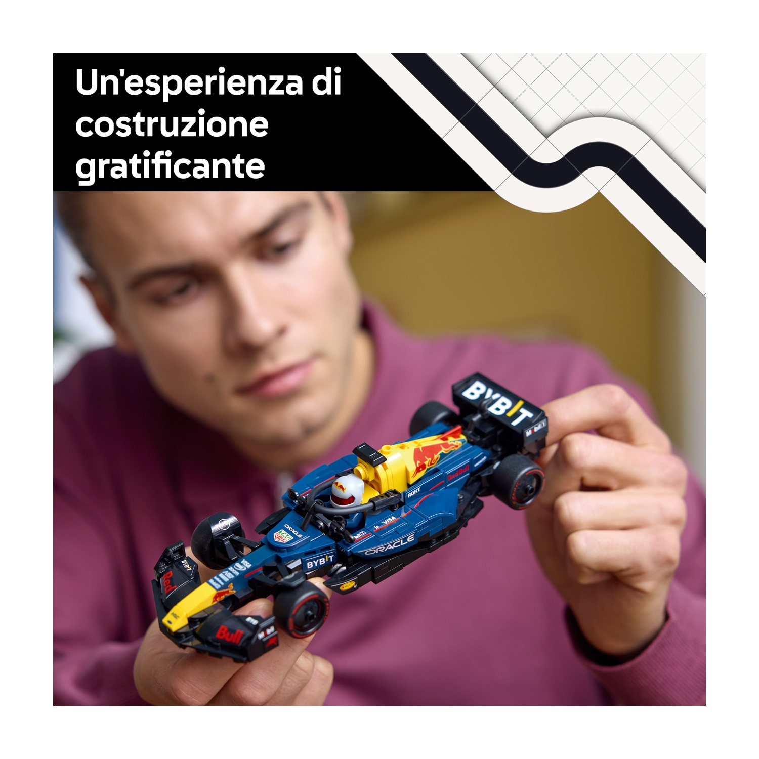 Una persona tiene in mano un piccolo modello di auto da corsa blu e gialla. Il modello ha i loghi degli sponsor. La persona indossa una camicia bordeaux.