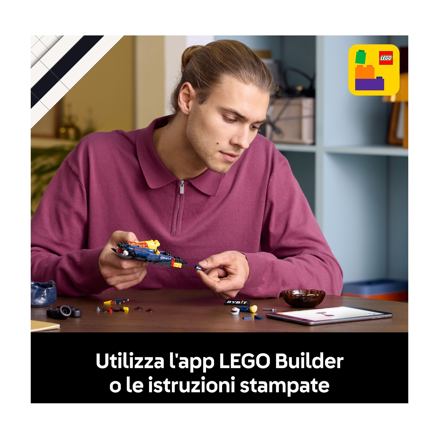 Un uomo assembla una macchina da corsa Lego. Indossa una camicia bordeaux ed è seduto a un tavolo di legno con pezzi Lego e un tablet.