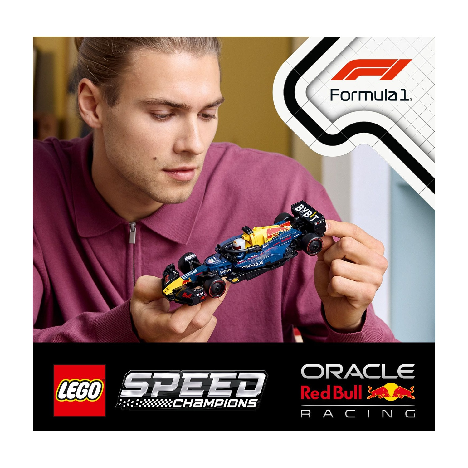 Un uomo tiene in mano una macchina di F1 Lego. L'auto è blu e gialla, con loghi degli sponsor. Lo sfondo presenta loghi e un logo Formula 1.