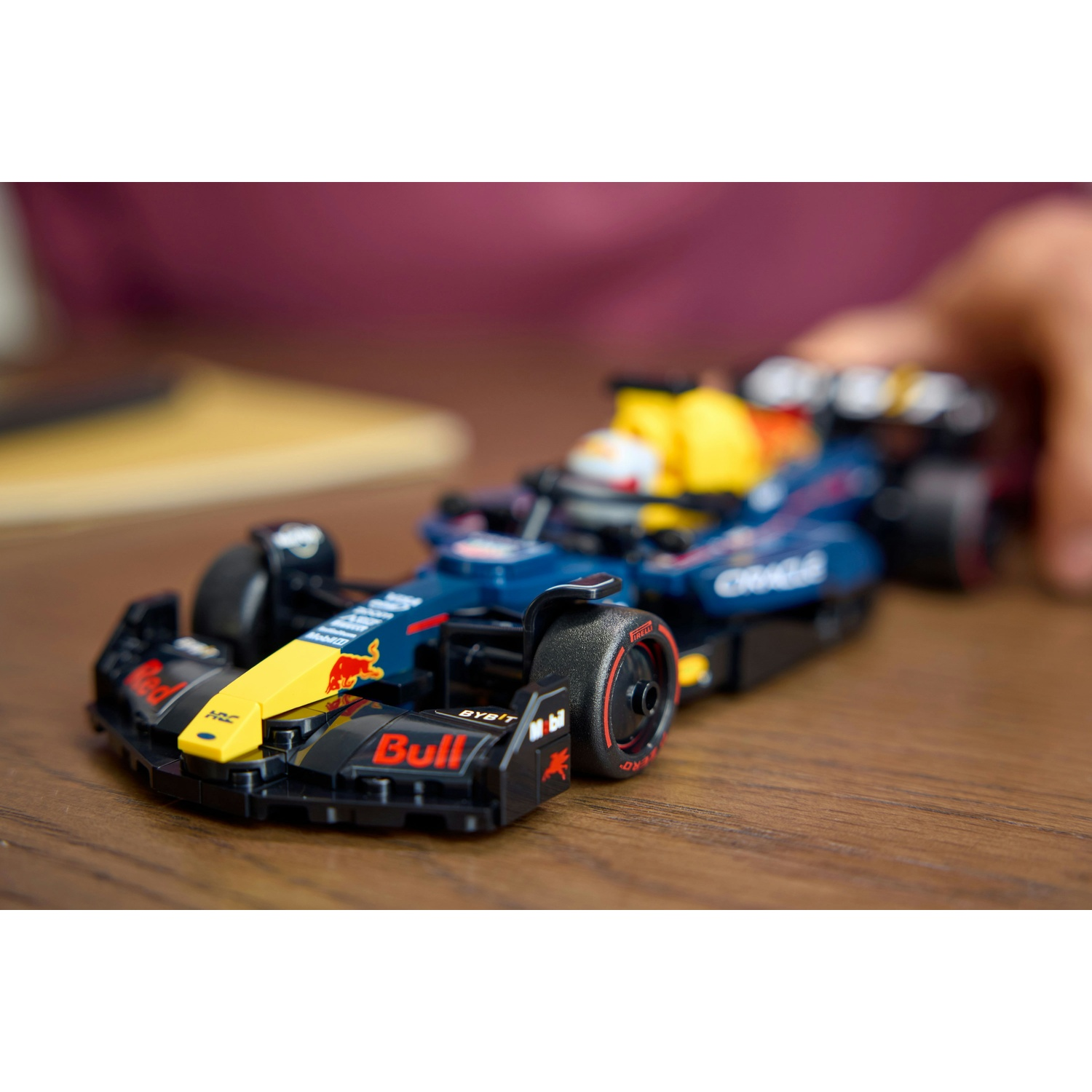 Un'auto giocattolo Red Bull di Formula 1 su una superficie di legno. Ha colori blu, giallo e nero. Una mano è visibile sullo sfondo.