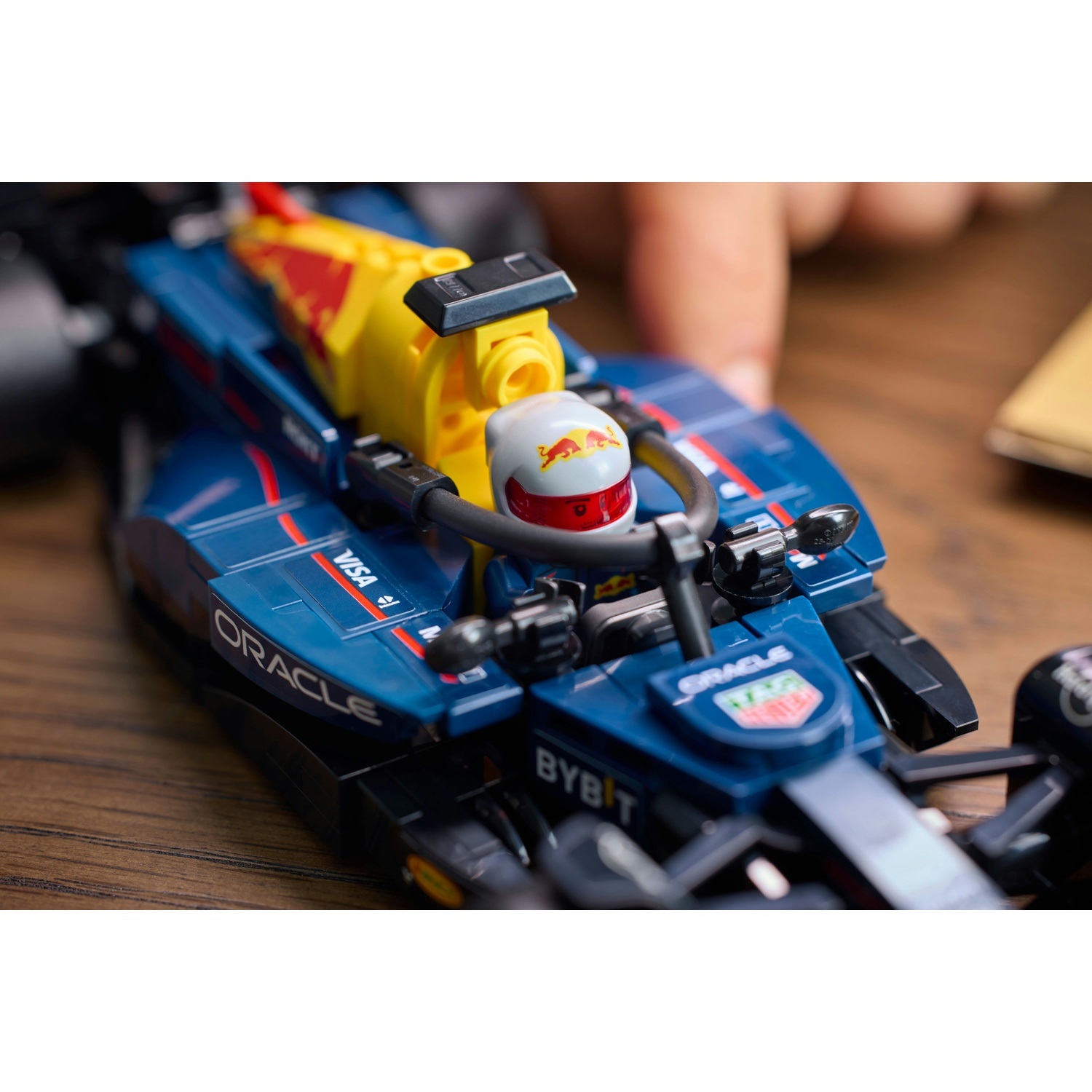 Primo piano di un'auto da corsa giocattolo blu e gialla con il logo Red Bull e un personaggio del pilota. Una mano è visibile vicino all'auto.