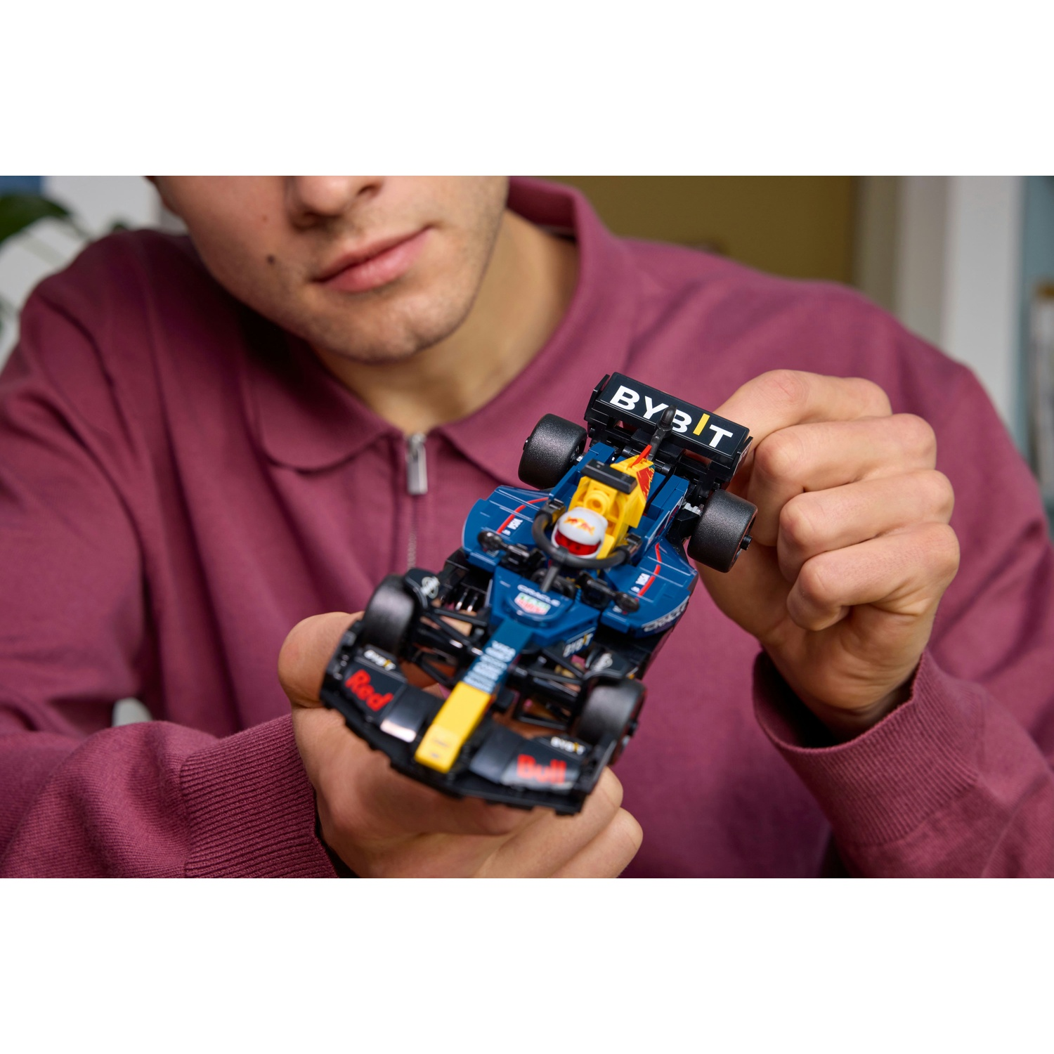 Una persona tiene in mano una piccola auto di Formula 1 Red Bull. L'auto è blu, nera e gialla. La persona indossa un maglione bordeaux.