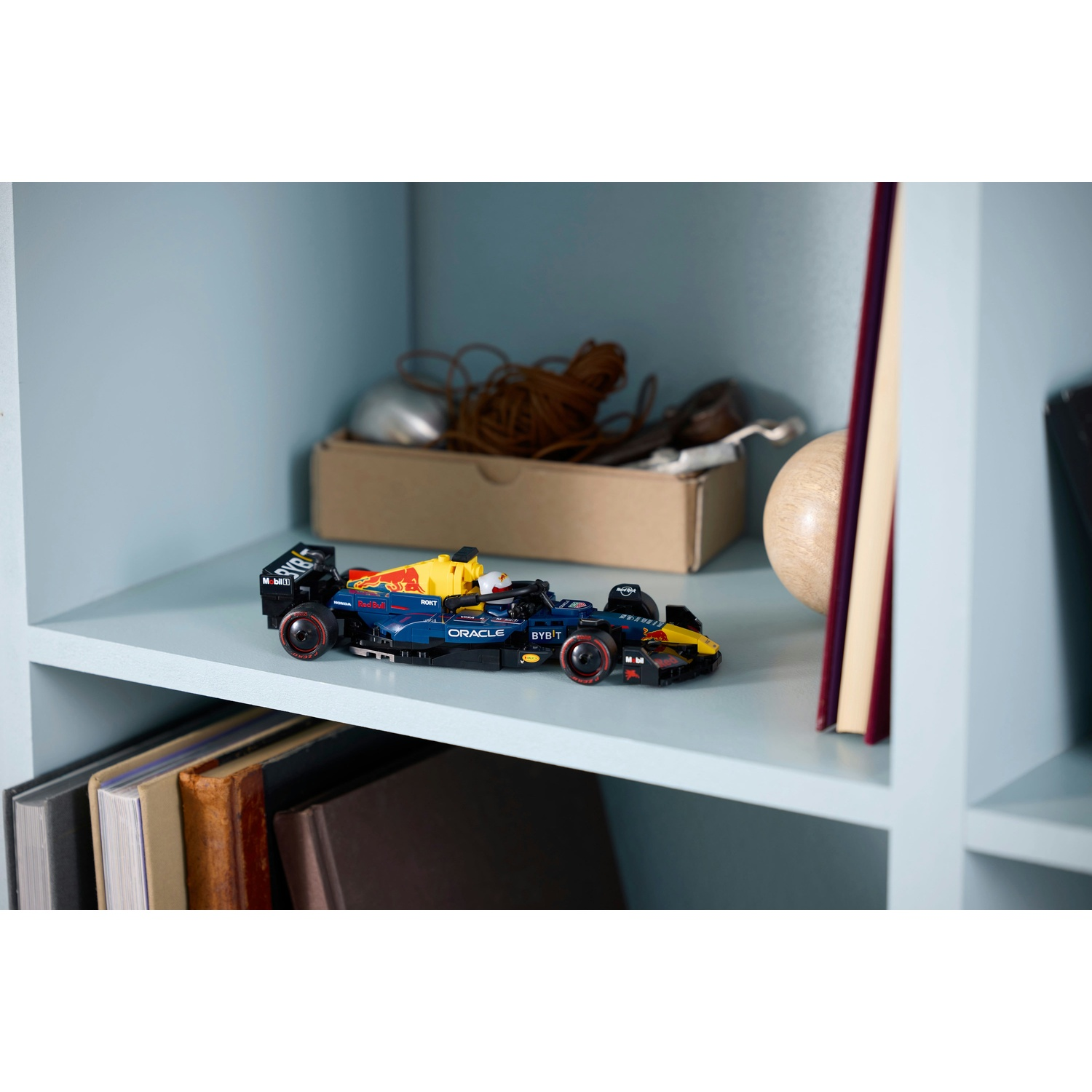Un'auto giocattolo di Formula 1 blu e gialla è su uno scaffale. Altri oggetti sullo scaffale includono libri, una palla di legno e una scatola.