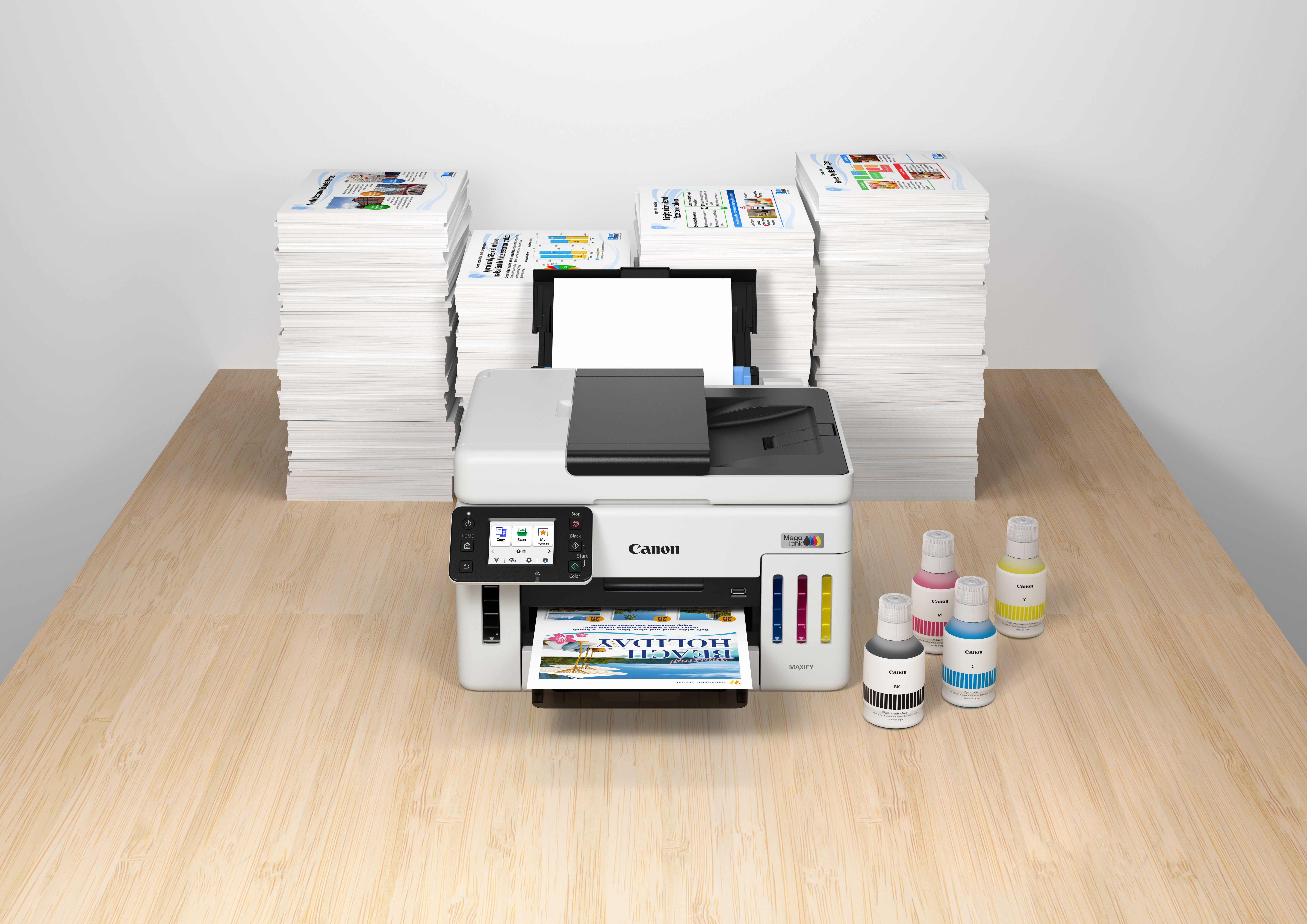 Ein Canon-Drucker mit Papierstapeln und Tintenflaschen auf einem Holztisch. Eine gedruckte Broschüre liegt im Ausgabefach.