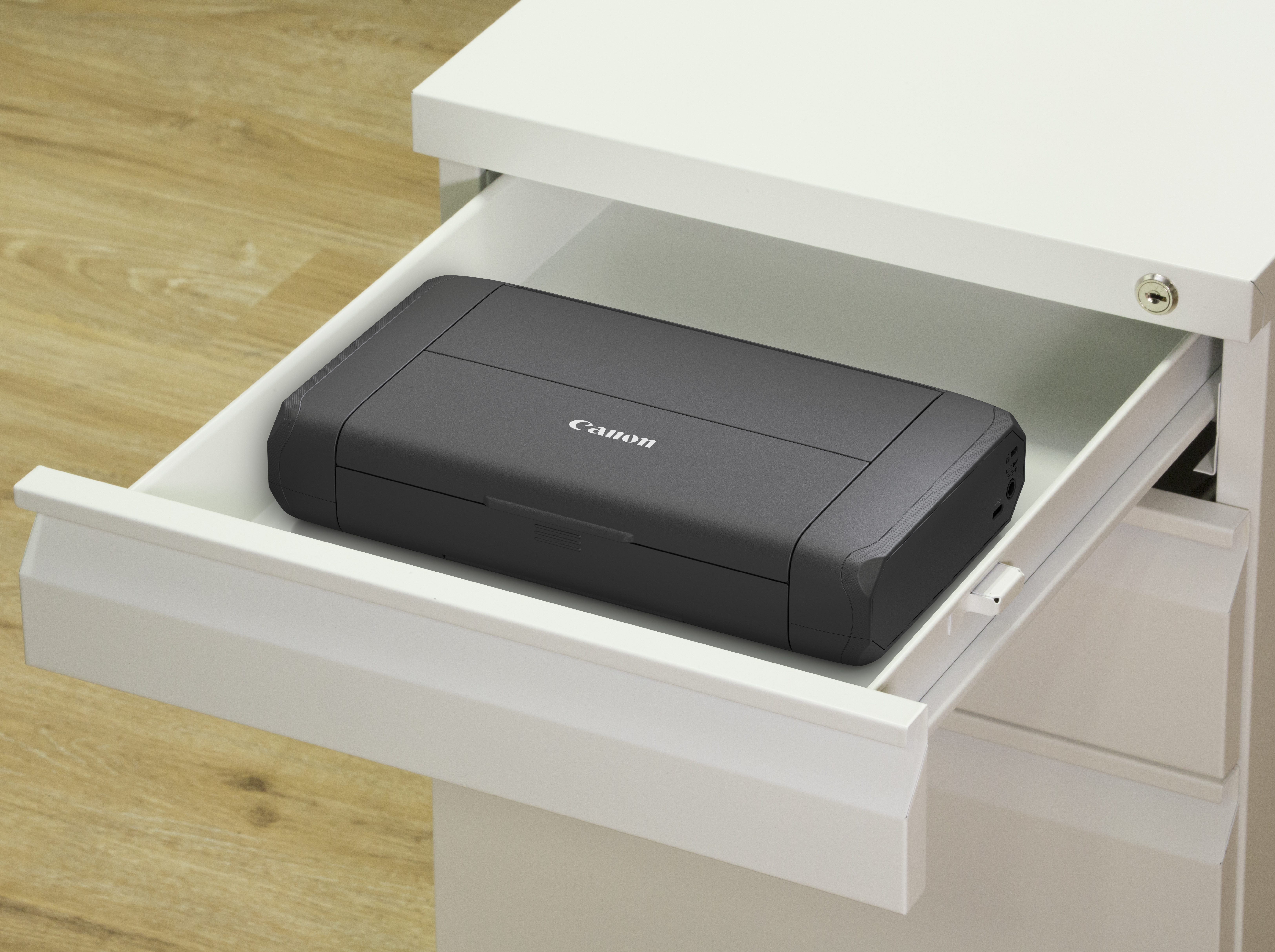 Una stampante Canon nera è in un cassetto bianco aperto. Il cassetto è in un mobile bianco su un pavimento di legno.