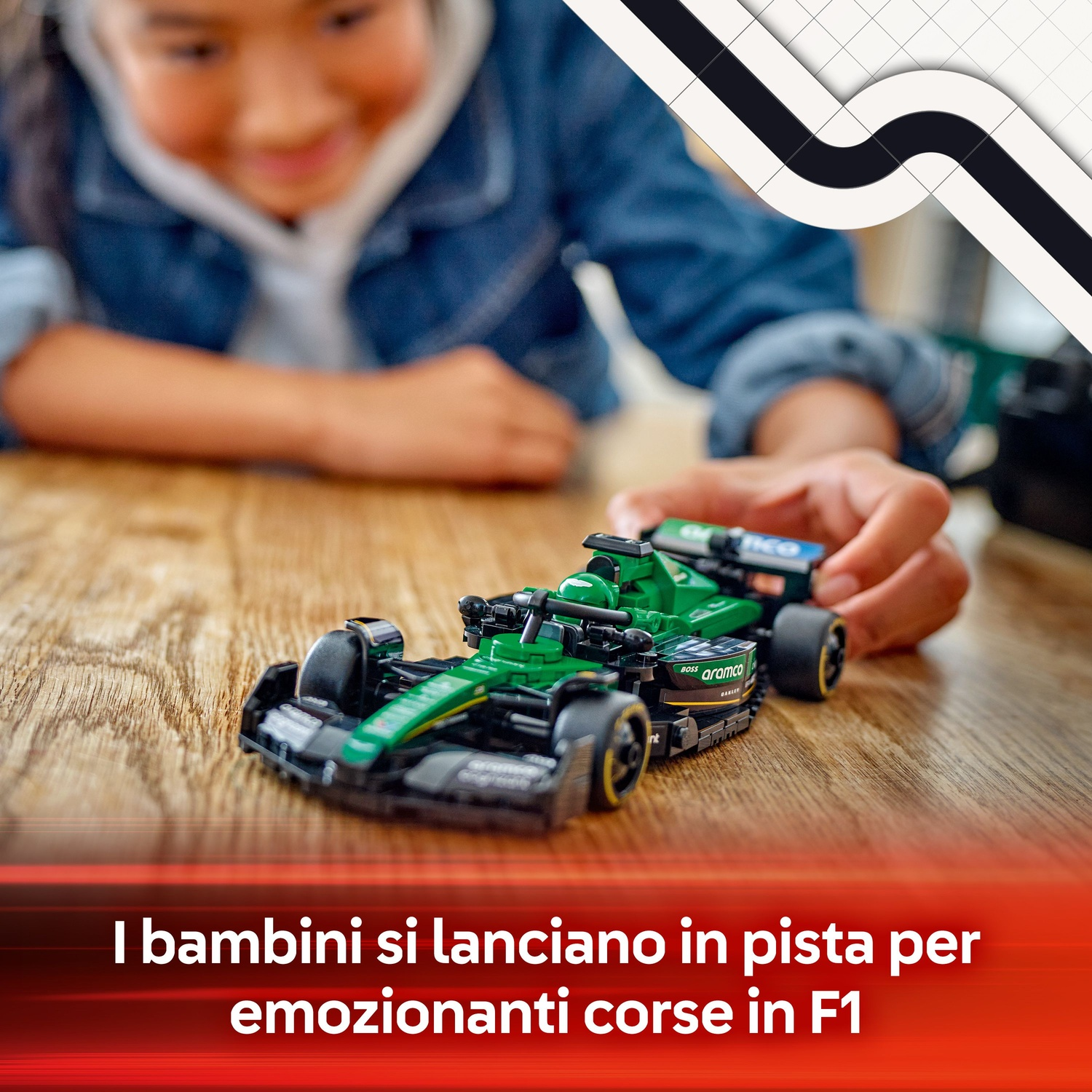 La mano di un bambino posiziona un'auto da corsa verde e nera su un tavolo di legno. L'auto ha i loghi degli sponsor. Il bambino è sfocato.