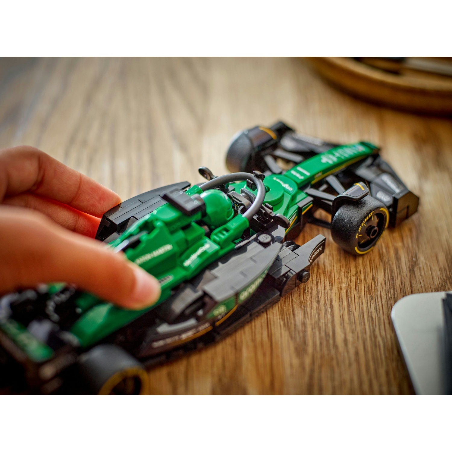 Una mano tocca un'auto da corsa giocattolo verde e nera su una superficie di legno. L'auto ha il numero 11 e un pilota all'interno.