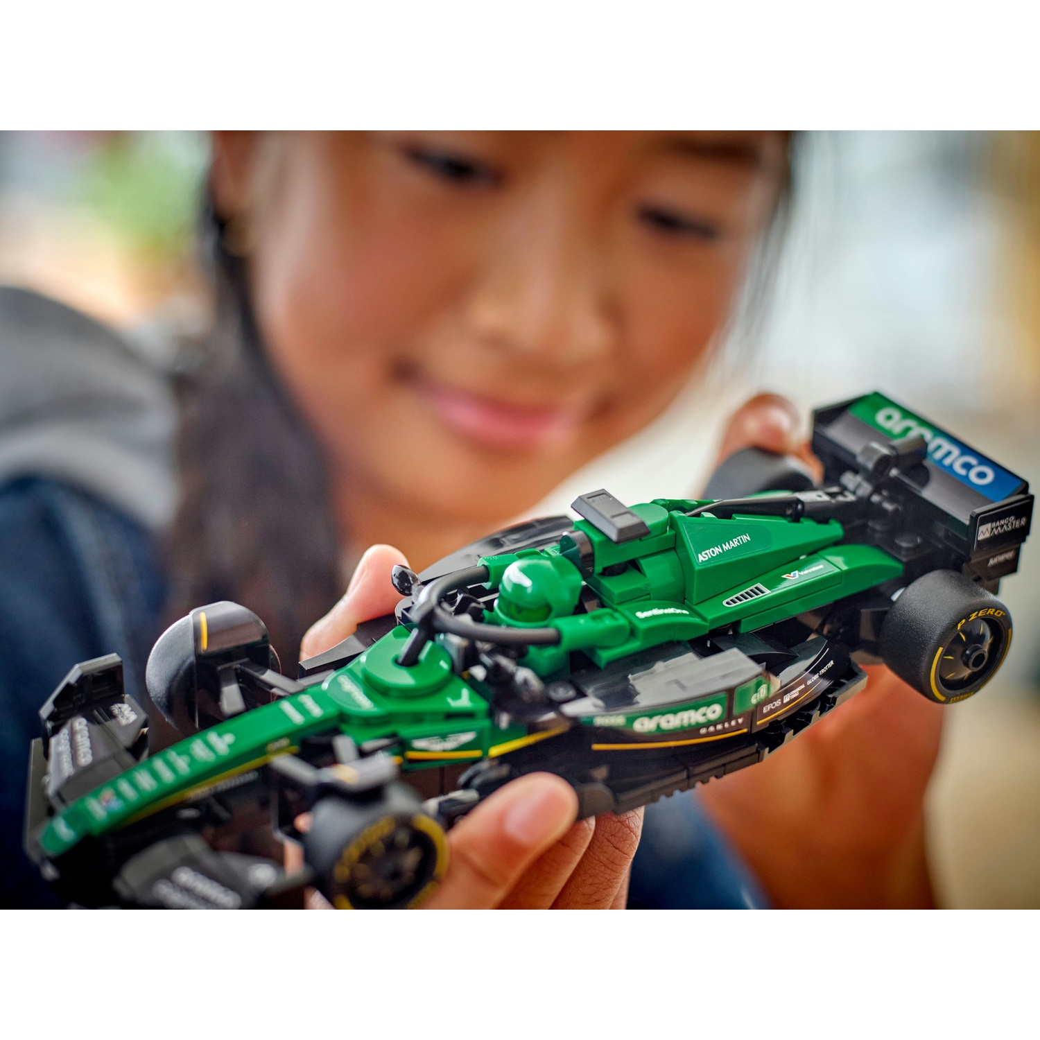 Una persona tiene in mano una macchina da corsa Lego verde e nera. L'auto ha i loghi degli sponsor e la persona sorride.