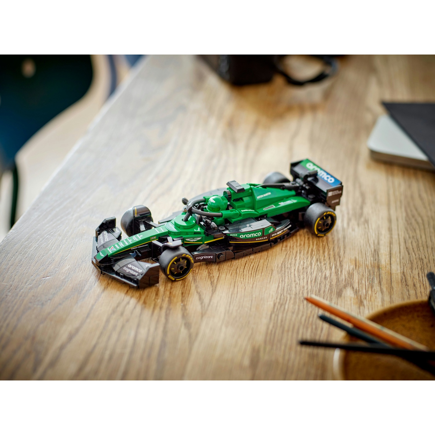 Un'auto da corsa giocattolo verde e nera è su un tavolo di legno. Sono presenti anche altri oggetti, come una ciotola e una penna.