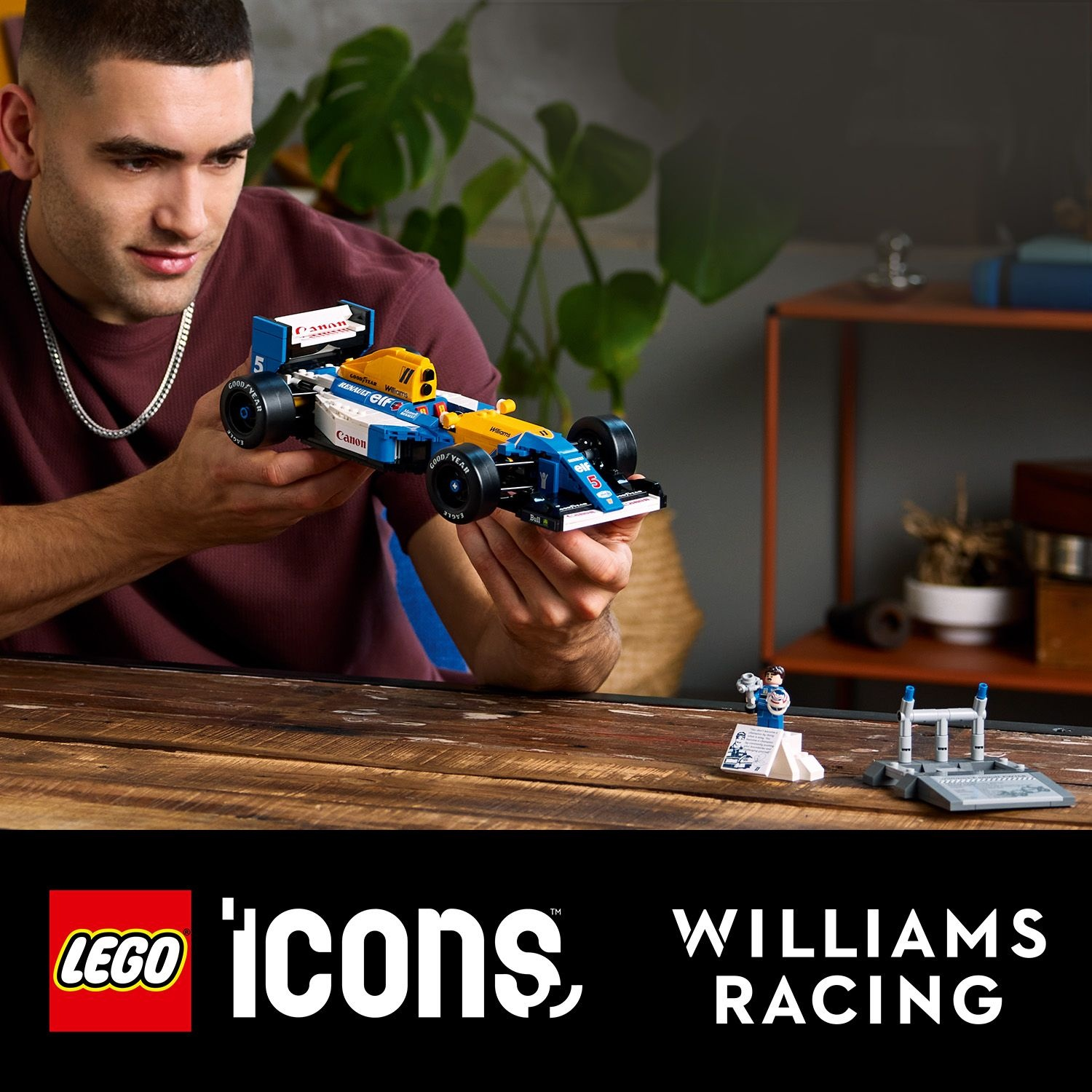 Un uomo tiene in mano un'auto da corsa LEGO Williams. L'auto è blu e gialla. Altri pezzi LEGO sono sul tavolo.