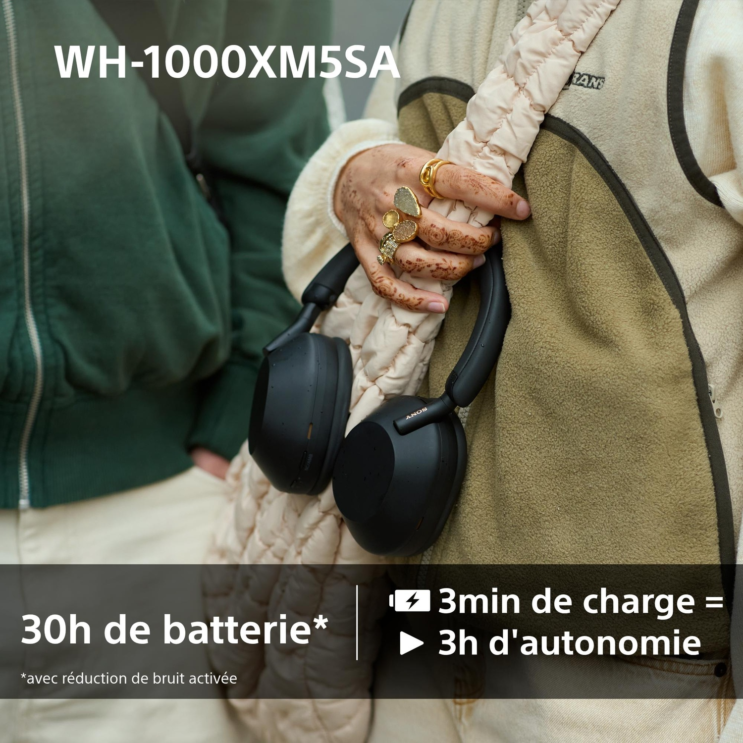 Personne tenant un casque noir. Le texte indique : 30h de batterie, 3min de charge = 3h d'autonomie. La personne porte des bagues et une veste.