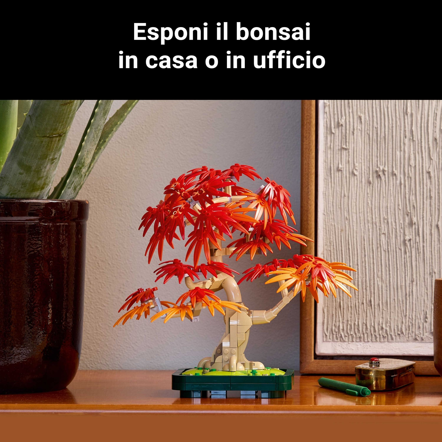 Un bonsai Lego con foglie rosse e arancioni è su una superficie di legno. A sinistra una pianta in un vaso marrone.