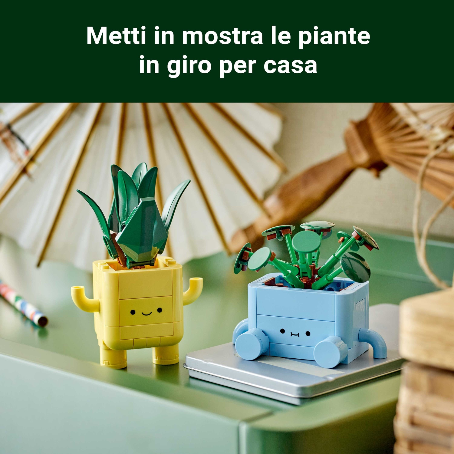 Due vasi Lego, giallo e blu, con piante verdi. Hanno facce da cartone animato. Sullo sfondo un ombrello di carta bianco.