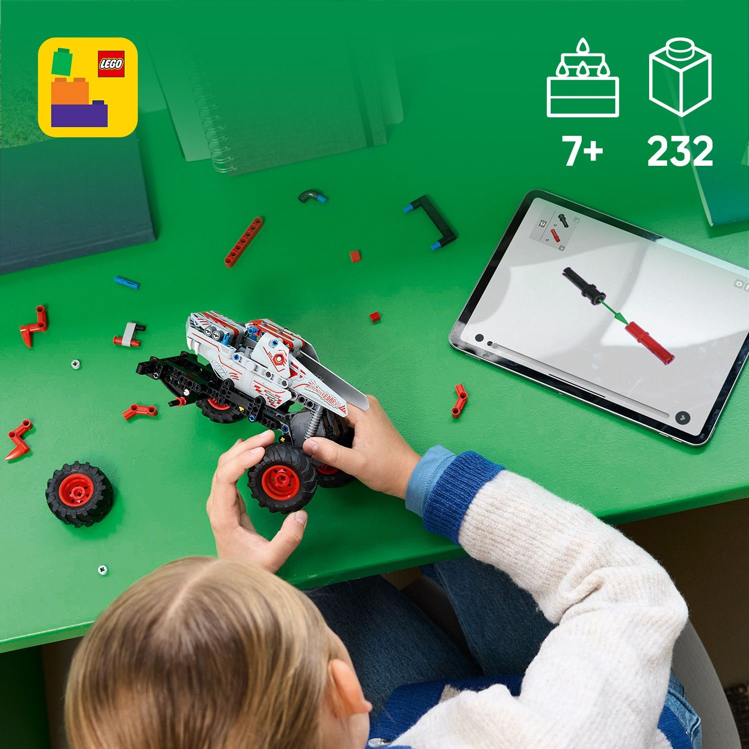 Un bambino sta assemblando un'auto Lego Technic su un tavolo verde, seguendo le istruzioni su un tablet. Parti e ruote sono sparse.