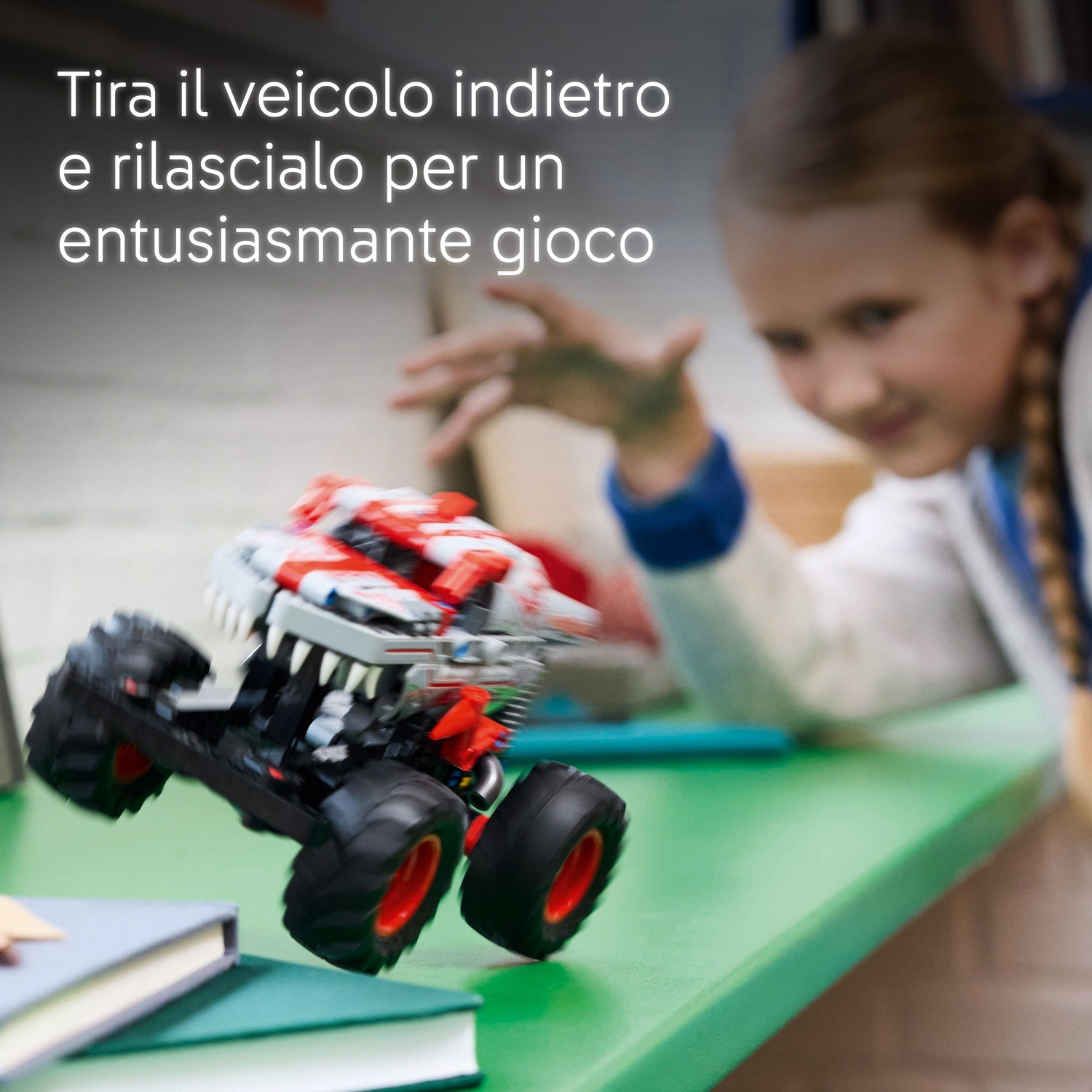 Un bambino gioca con un camion mostro giocattolo. Il camion è rosso, bianco e nero. I libri sono su una superficie verde.