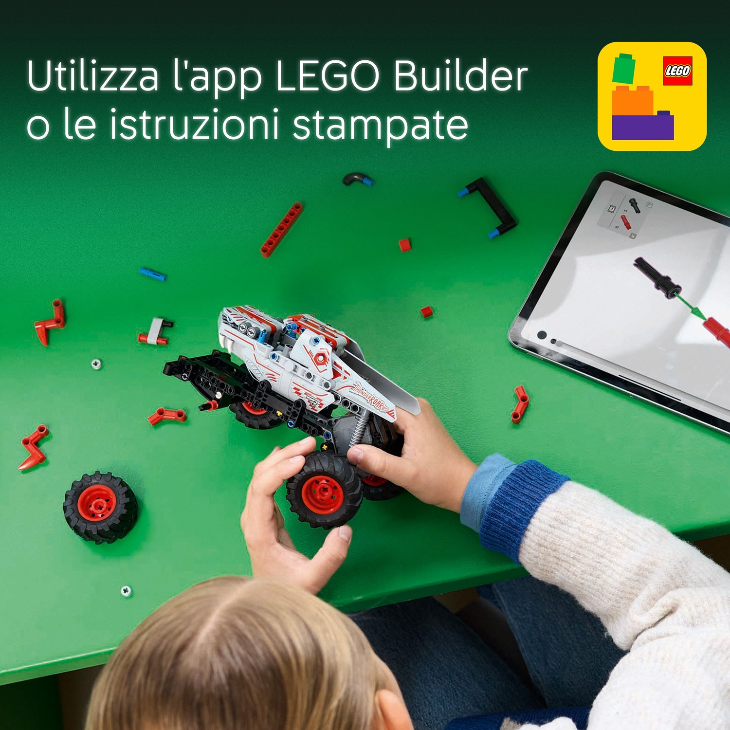 Un bambino assembla un'auto Lego Technic su una superficie verde, usando le istruzioni su un tablet. Vari pezzi Lego sono sparsi.