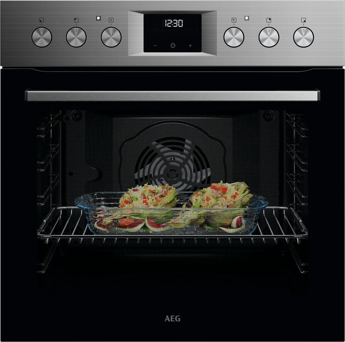Ein Backofen mit Essen darin. Der Ofen ist aus Edelstahl. Zwei Hälften von gebackenen Artischocken in einer Glasschale.