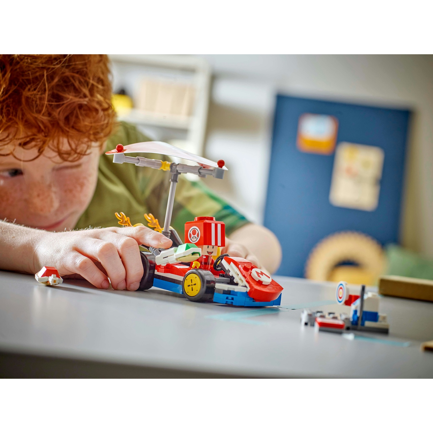 Un bambino gioca con un set Lego di Mario Kart. Il set include un kart rosso e blu con un ombrello bianco.