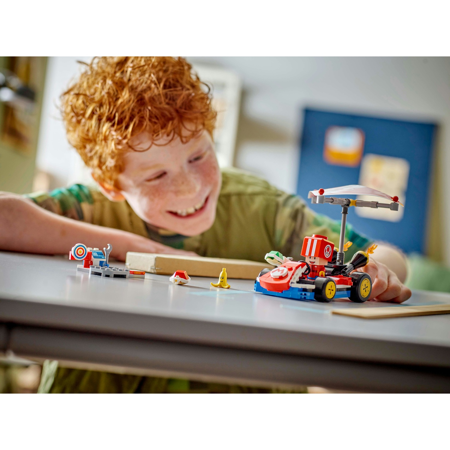Un ragazzo sorridente guarda un set Lego, con un kart rosso e blu, accessori e un piccolo bersaglio.