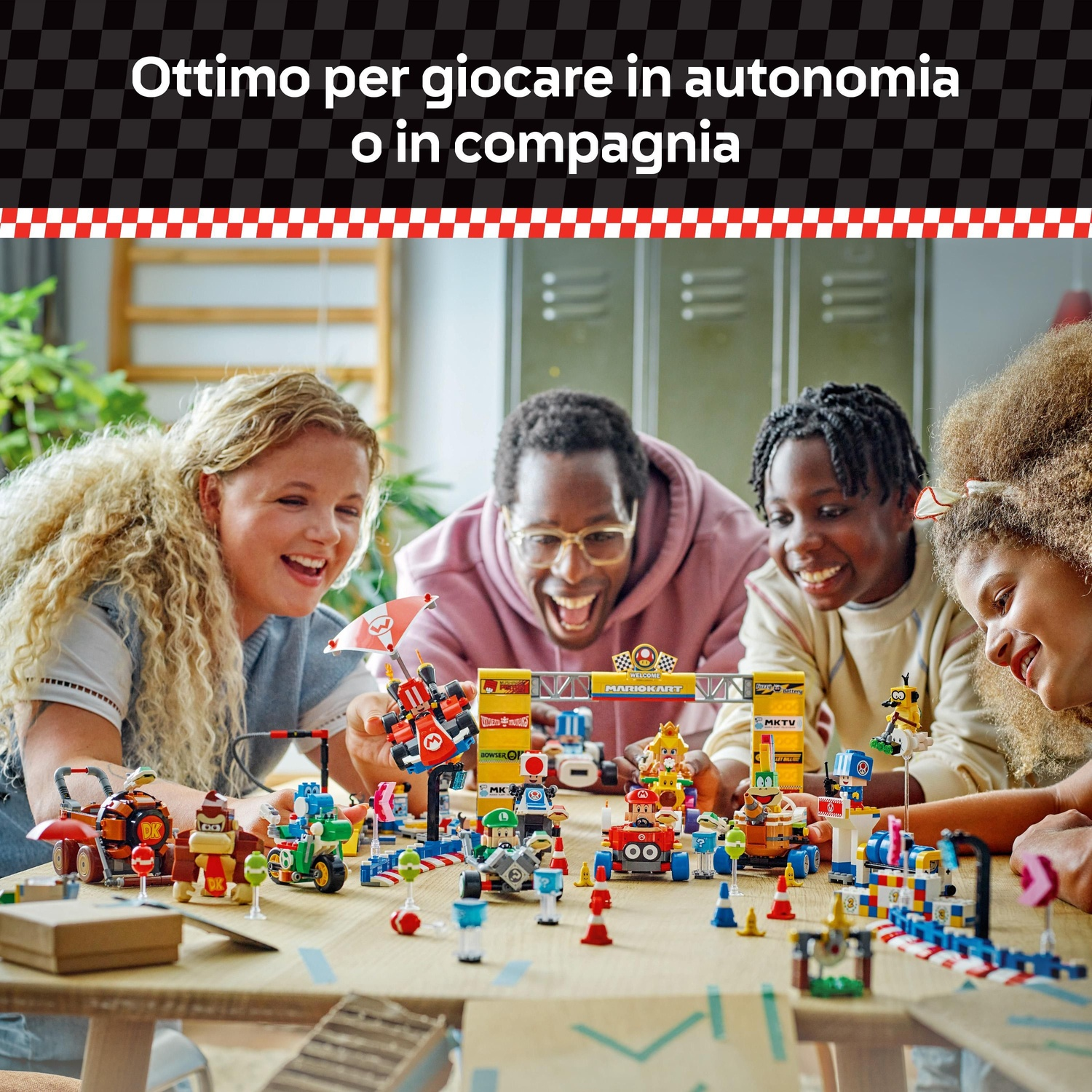 Quattro persone giocano con i giocattoli di Mario Kart su un tavolo di legno. La scena include vari personaggi giocattolo e un circuito di gara.