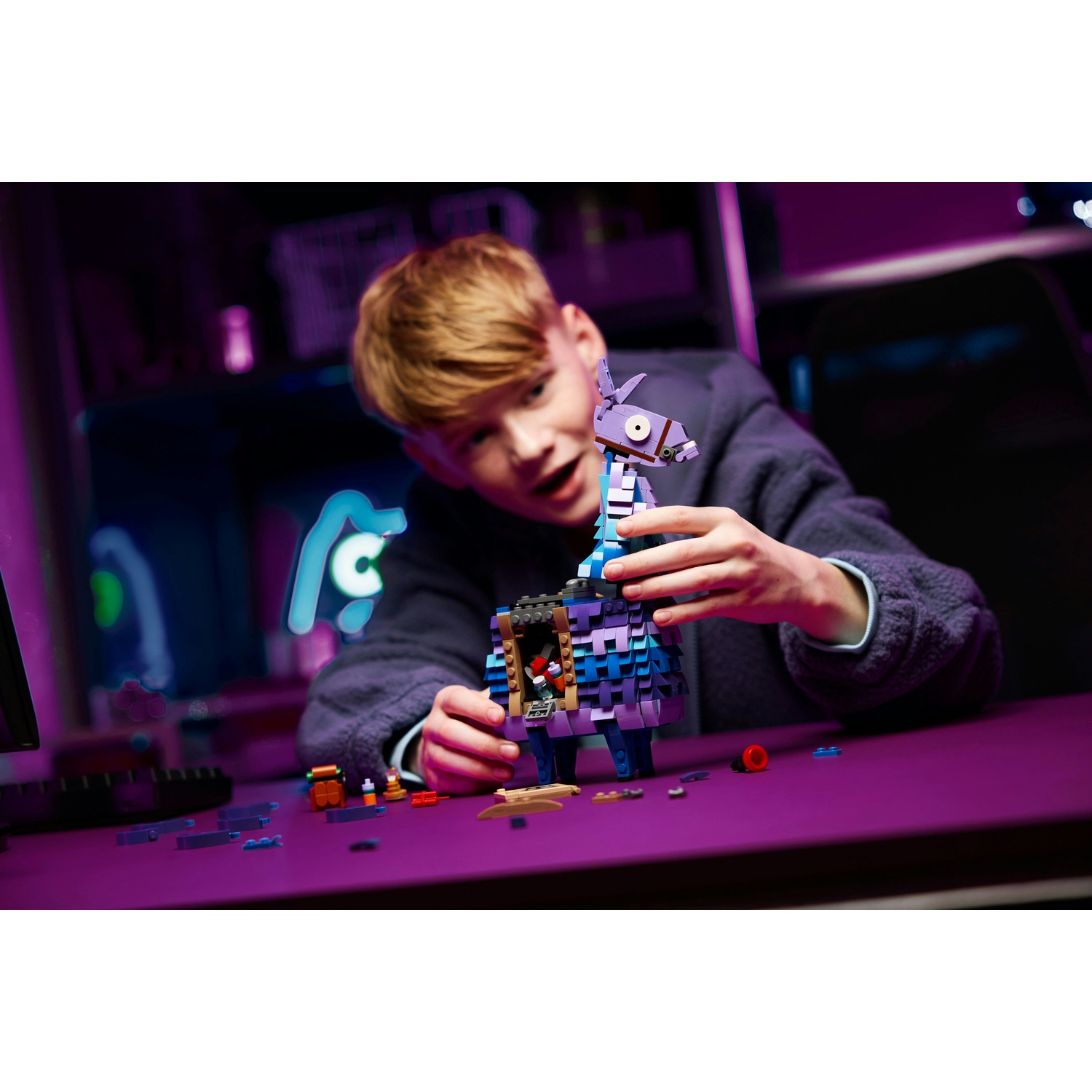 Un ragazzo assembla un lama Lego su un tavolo viola. La scena è illuminata da luci viola e blu.