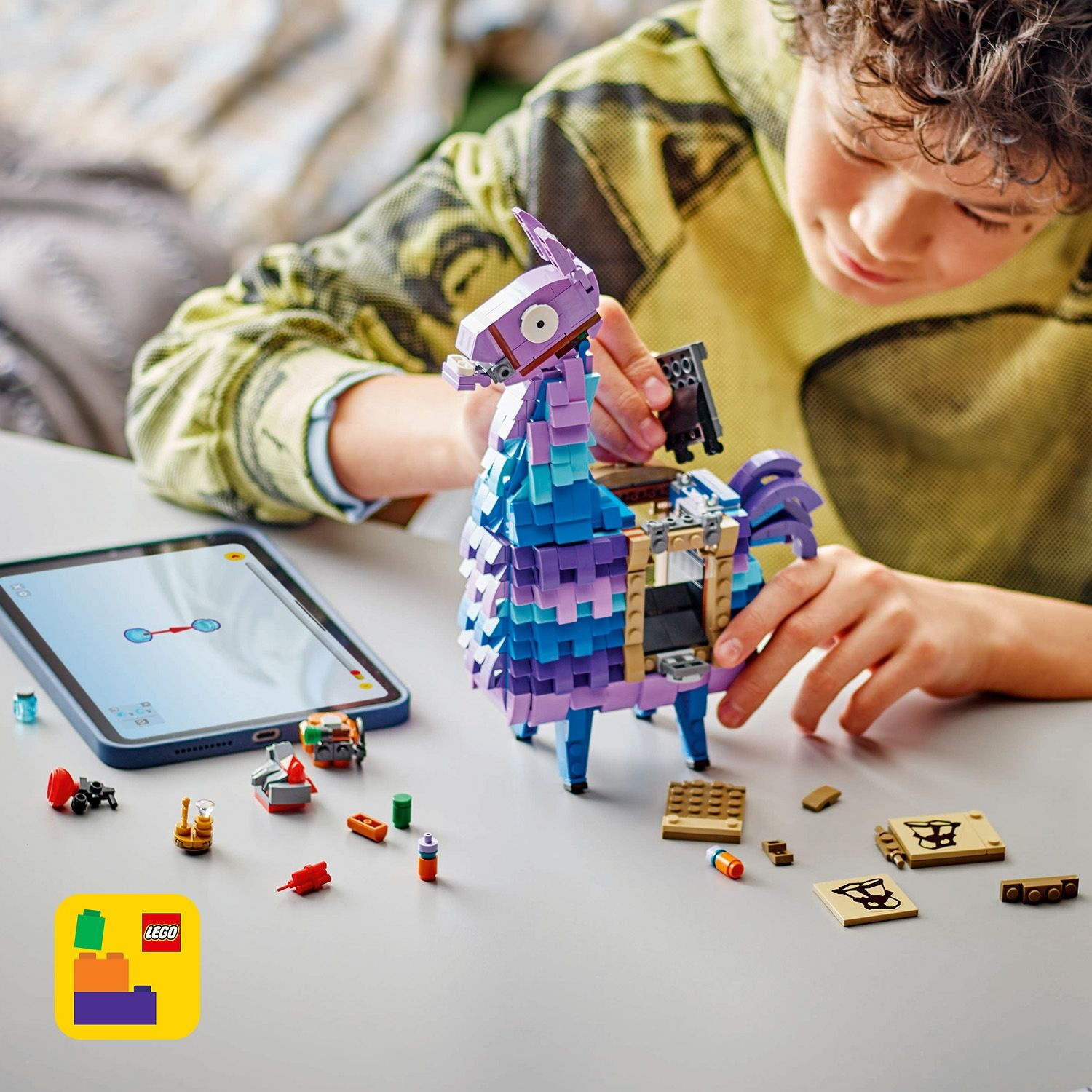 Un bambino assembla un lama Lego con un tablet e pezzi Lego su un tavolo. Il lama è blu, viola e bianco.
