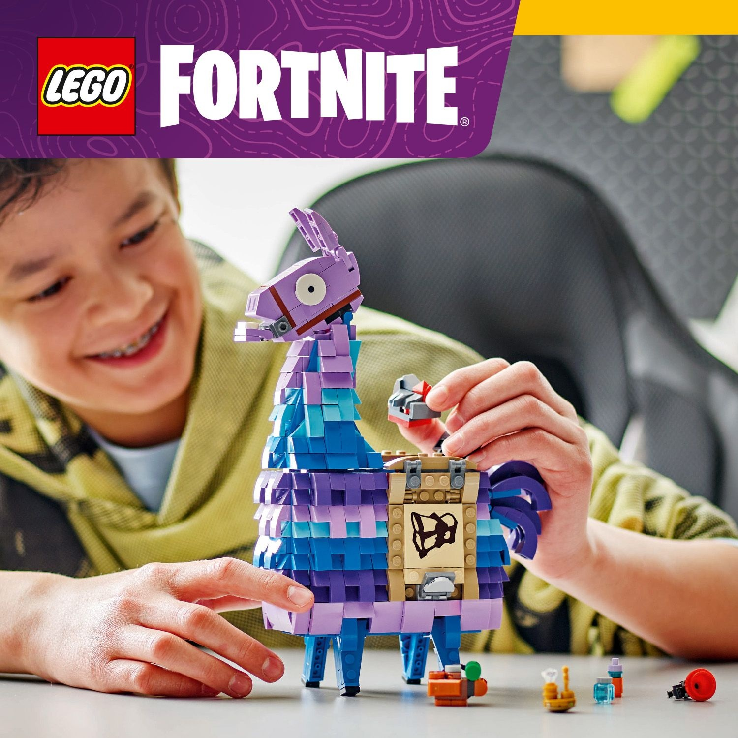 Un ragazzo sorride mentre assembla un set LEGO Fortnite lama. Il lama è viola e blu. Ci sono altri pezzi LEGO nelle vicinanze.