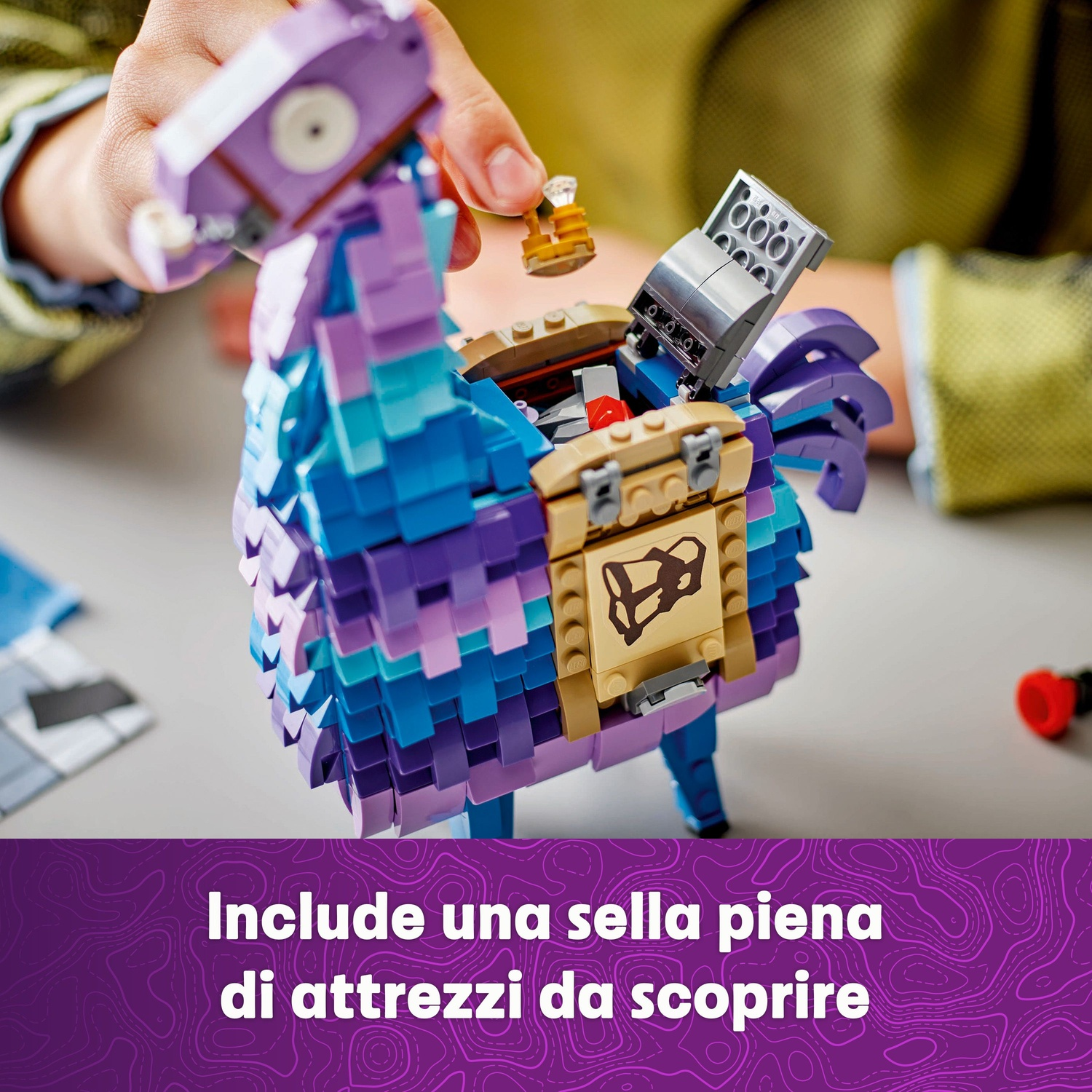 Una persona apre una scatola Lego a forma di lama colorata. La scatola è blu, viola e verde acqua. Vengono inseriti piccoli oggetti d'oro.