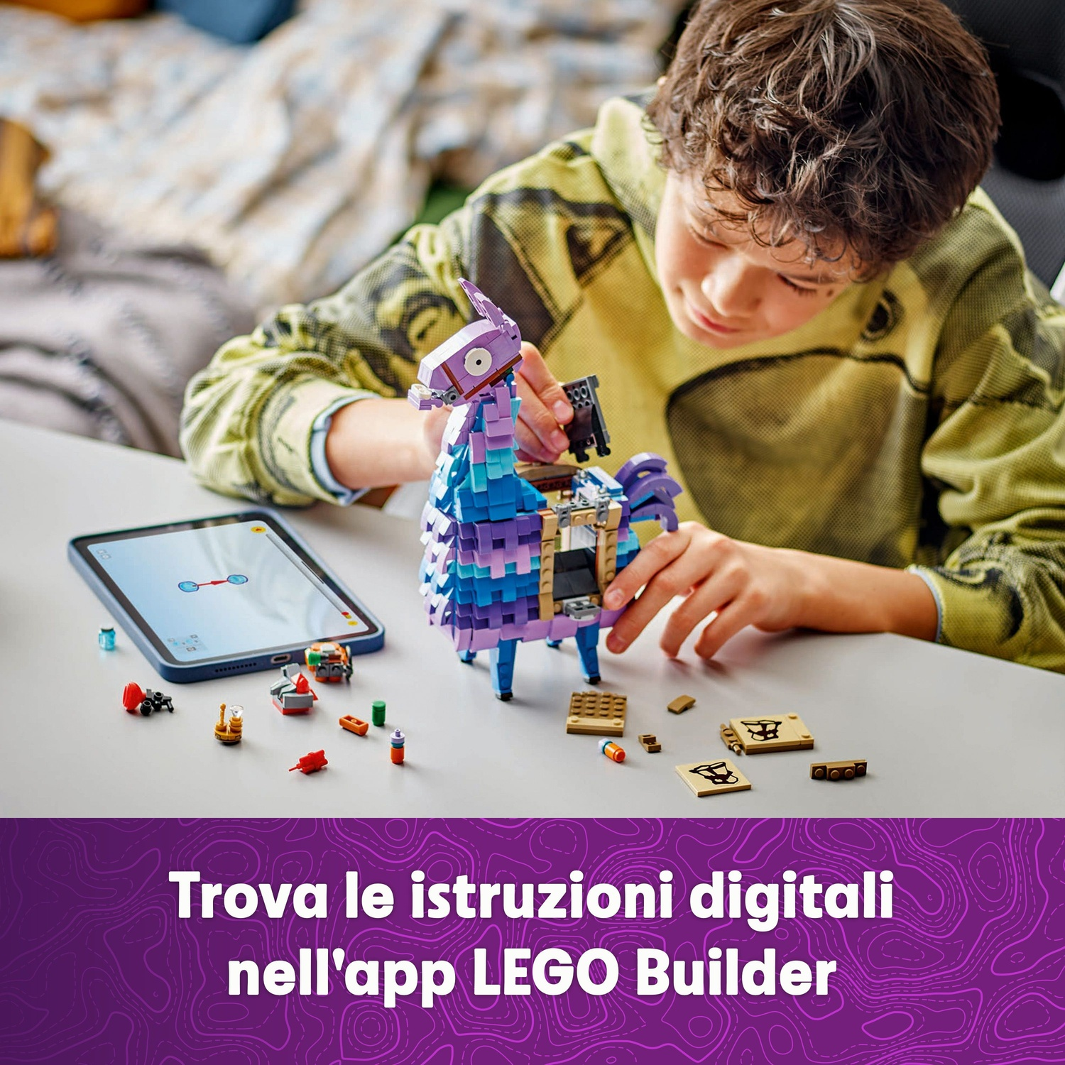Un ragazzo costruisce un lama Lego. Un tablet mostra le istruzioni. I pezzi Lego sono sparsi su un tavolo bianco. Lo sfondo è sfocato.