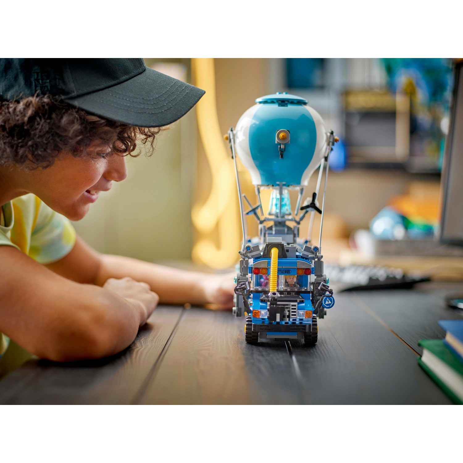Una persona guarda un set Lego di mongolfiera e veicolo blu e bianco su una scrivania di legno. Viene indossato un berretto nero.