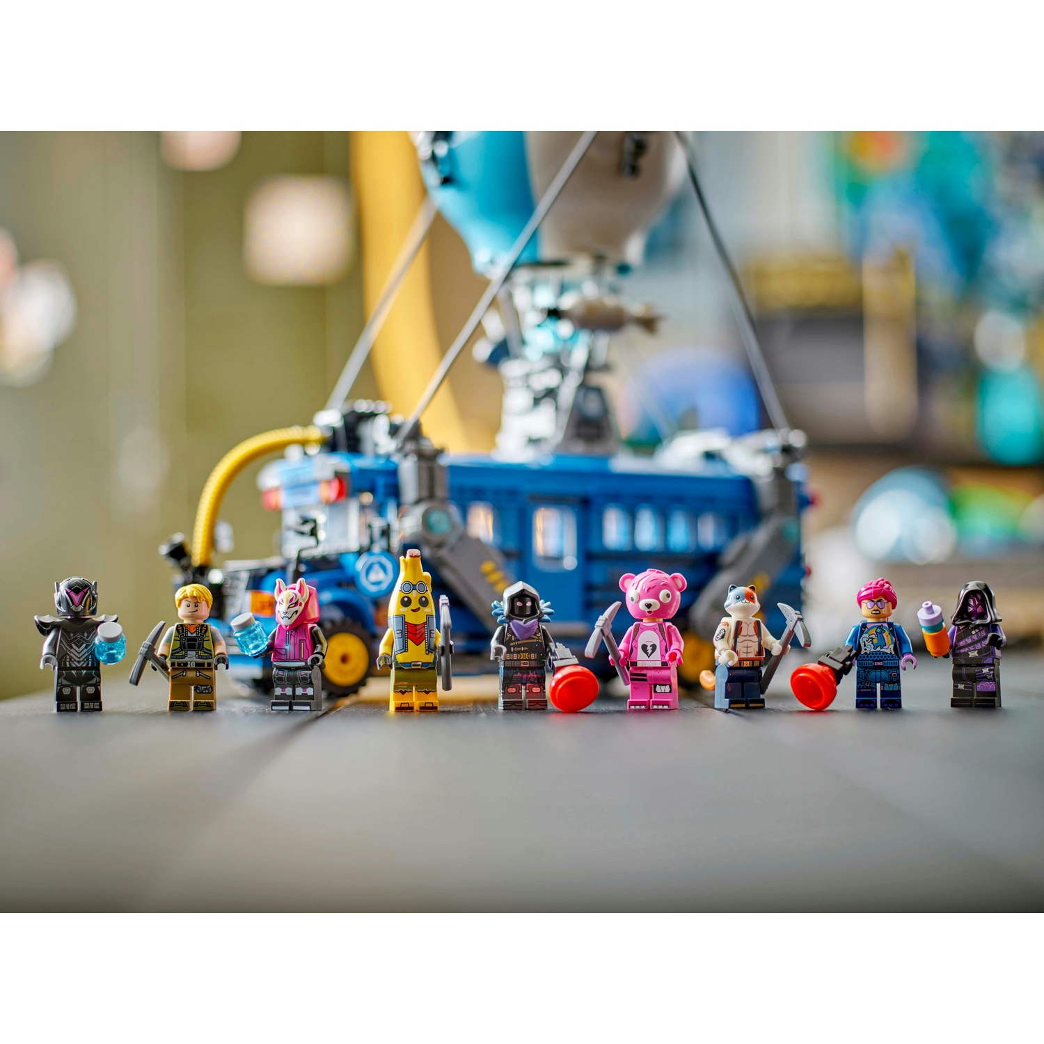 Figurine Lego di vari personaggi, tra cui una banana, un orso e altri, in piedi di fronte a un autobus blu e a un dirigibile.
