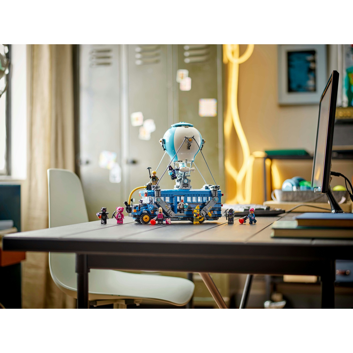 Un set Lego con un autobus blu con un palloncino sopra, circondato da personaggi Lego su una scrivania scura. Lo sfondo ha degli armadietti.