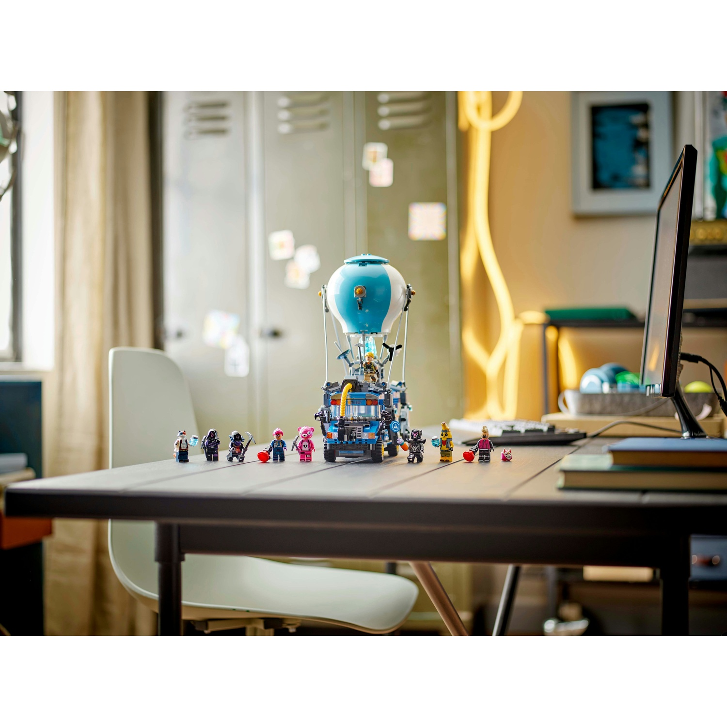 Un set Lego con una mongolfiera blu e bianca con figurine su una scrivania, con un computer e altri oggetti sullo sfondo.