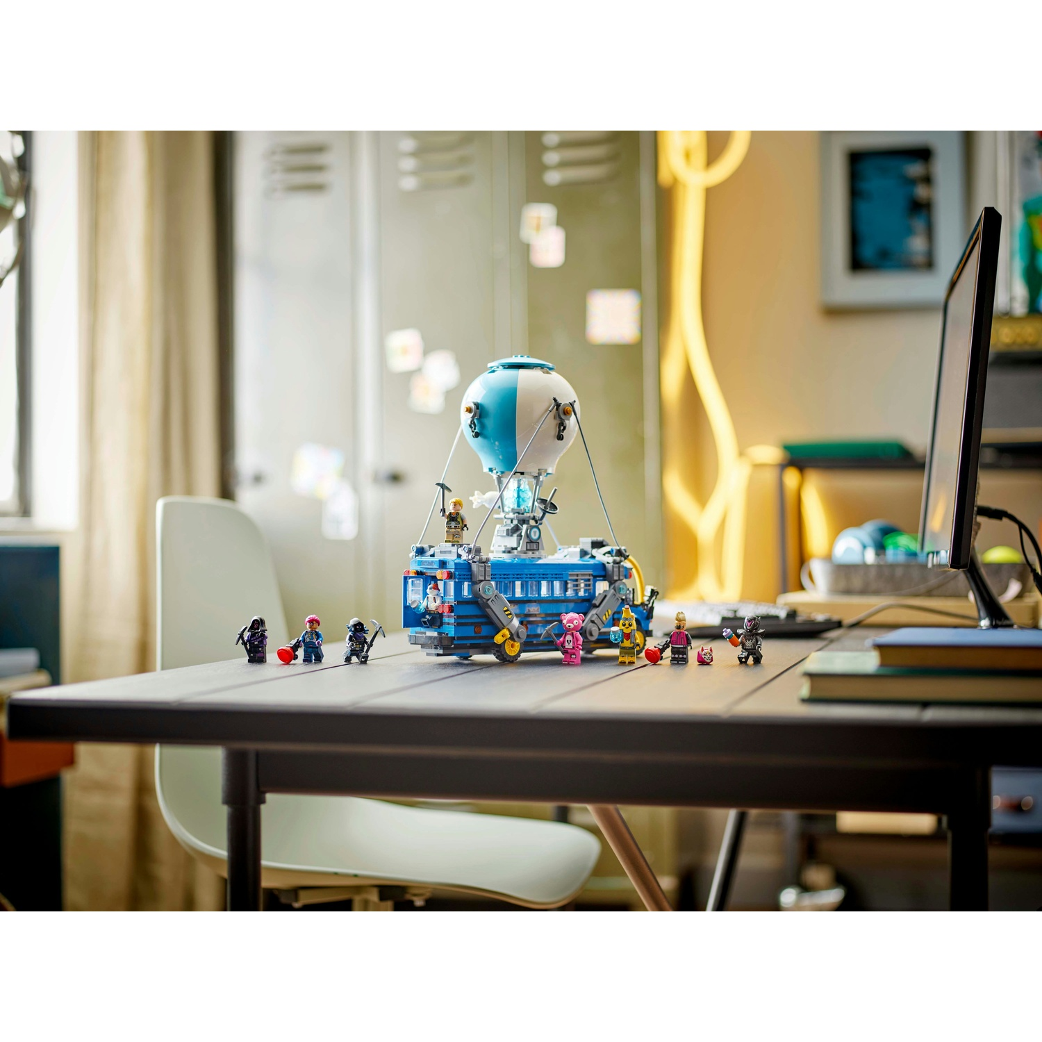 Un set Lego con un autobus blu con un palloncino sopra, circondato da personaggi Lego, su un tavolo nero con una sedia bianca.