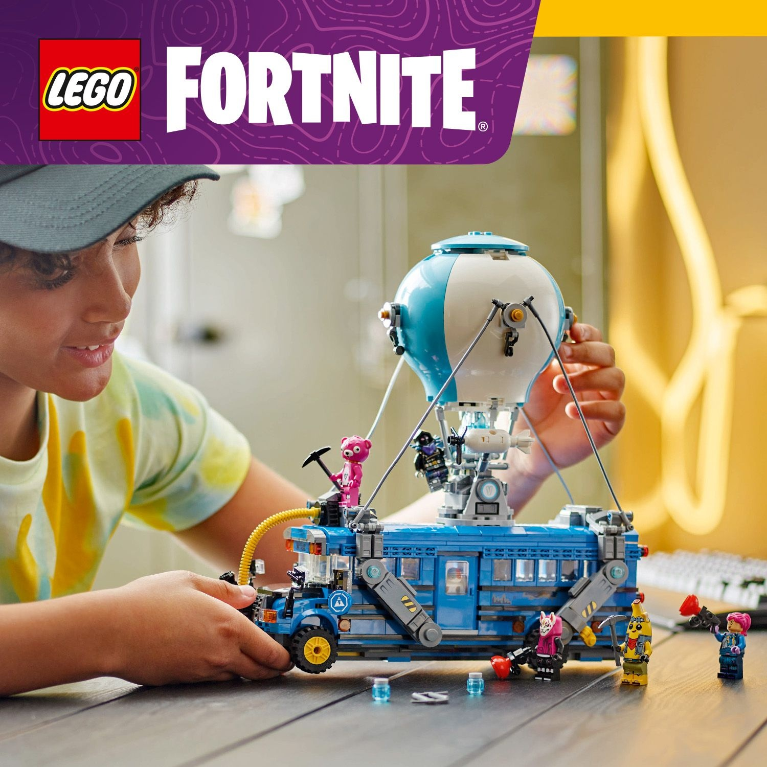 Un bambino gioca con un set Lego Fortnite. Presenta un autobus blu con un pallone, minifigure e accessori. Il logo Lego è visibile.
