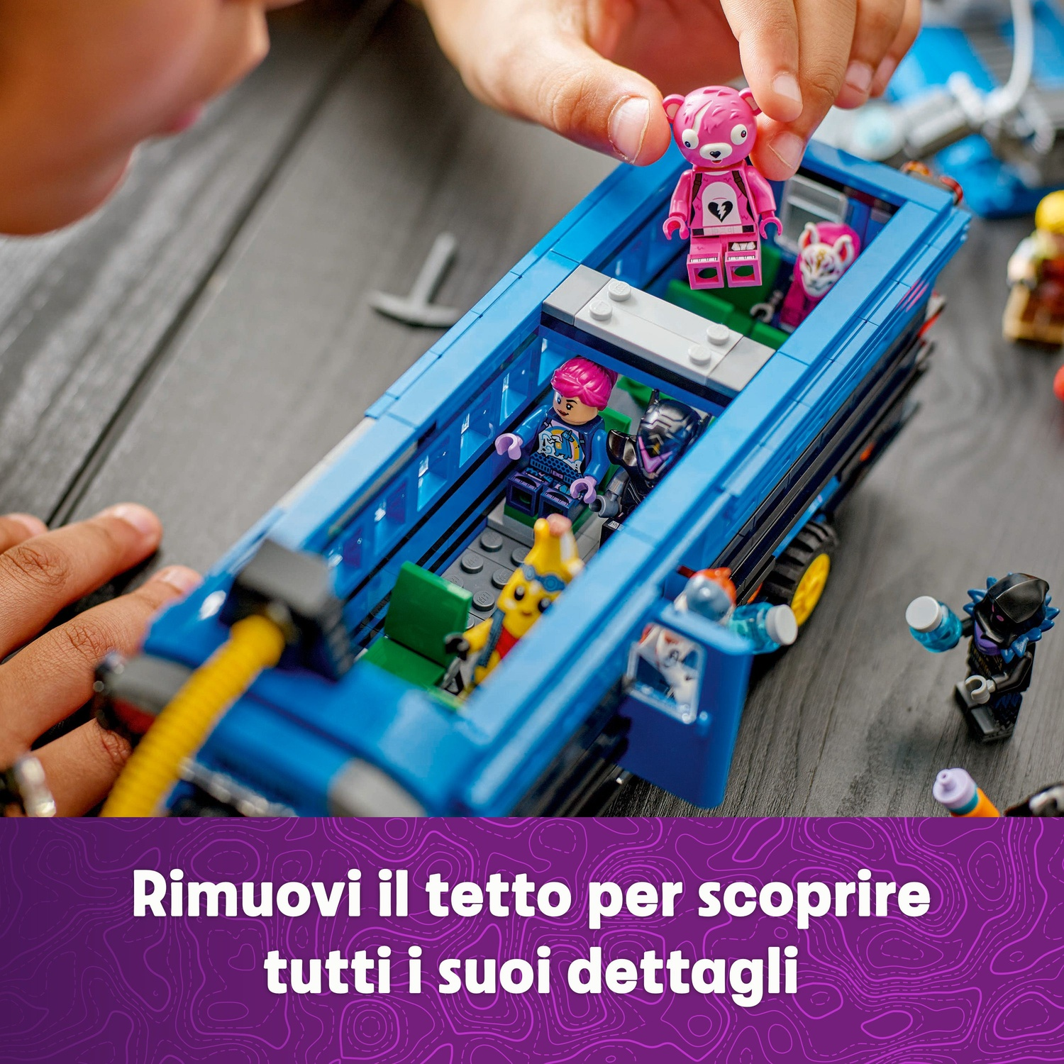 Le mani di un bambino tengono un orsetto rosa Lego sopra un autobus Lego blu. Altre figure Lego sono all'interno dell'autobus.