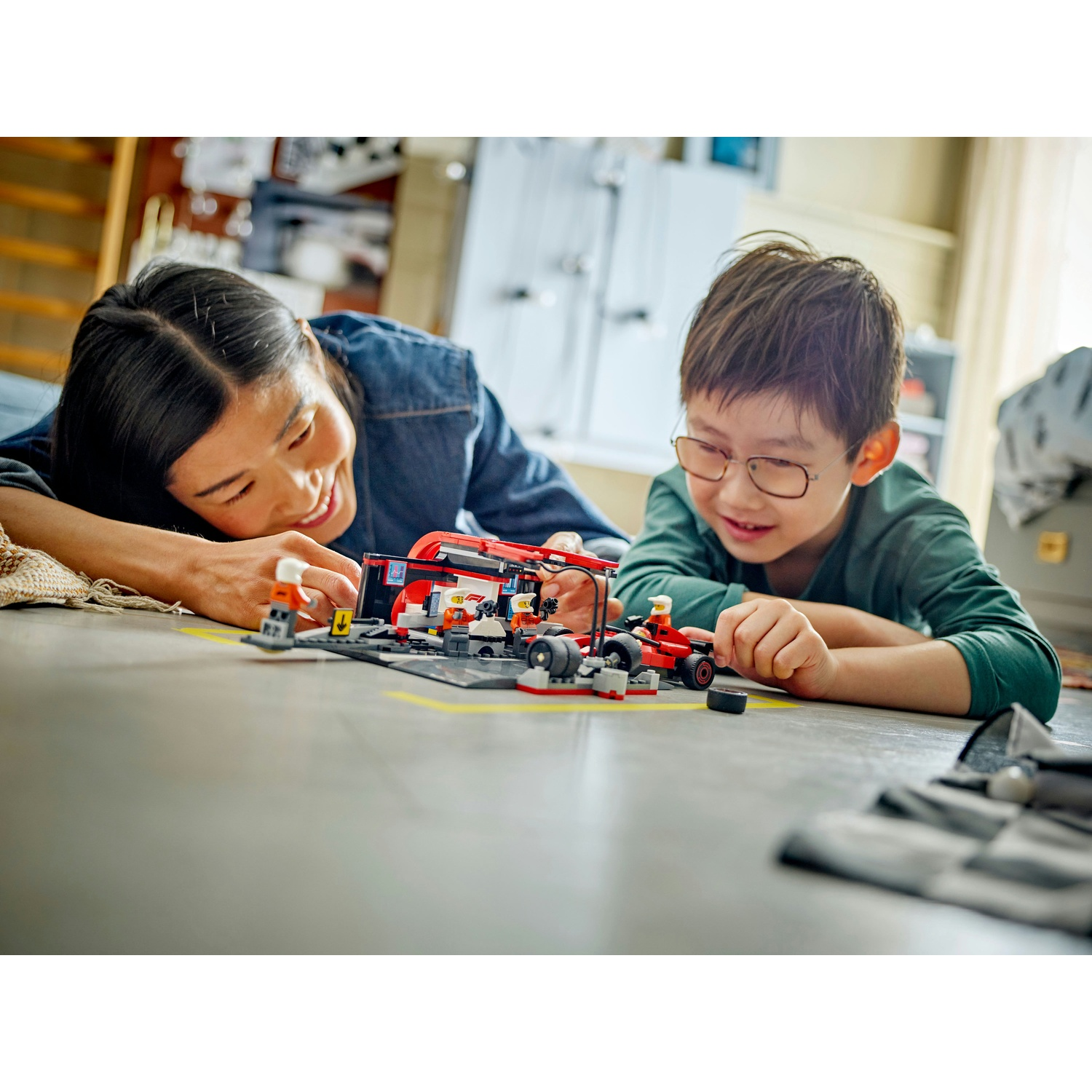 Una donna e un bambino giocano con un set di auto da corsa Lego. Sono sdraiati sul pavimento, sorridono e guardano i giocattoli.