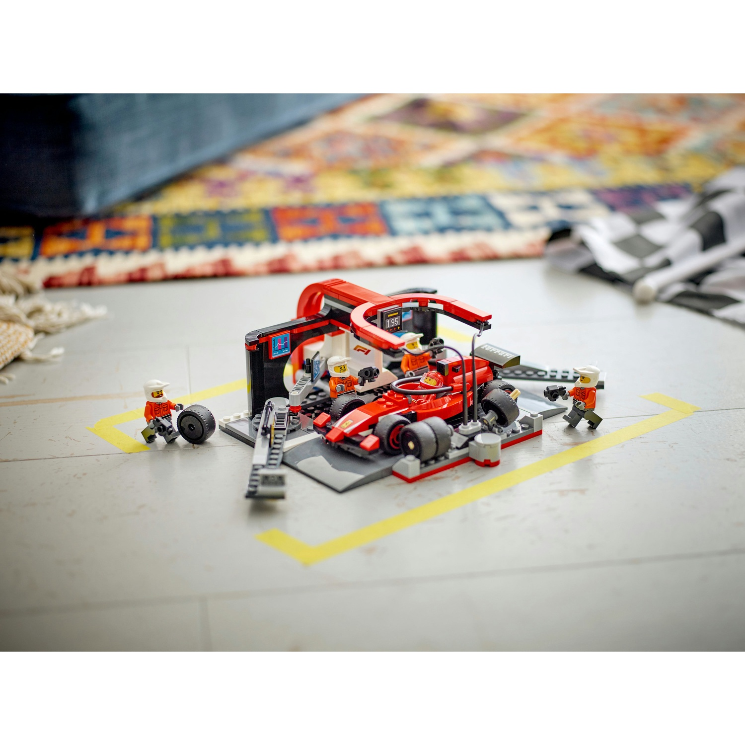 Un'auto da corsa Lego e un team di box sono su un pavimento grigio. Un'auto rossa è al centro. Personaggi Lego e una bandiera a scacchi sono sullo sfondo.