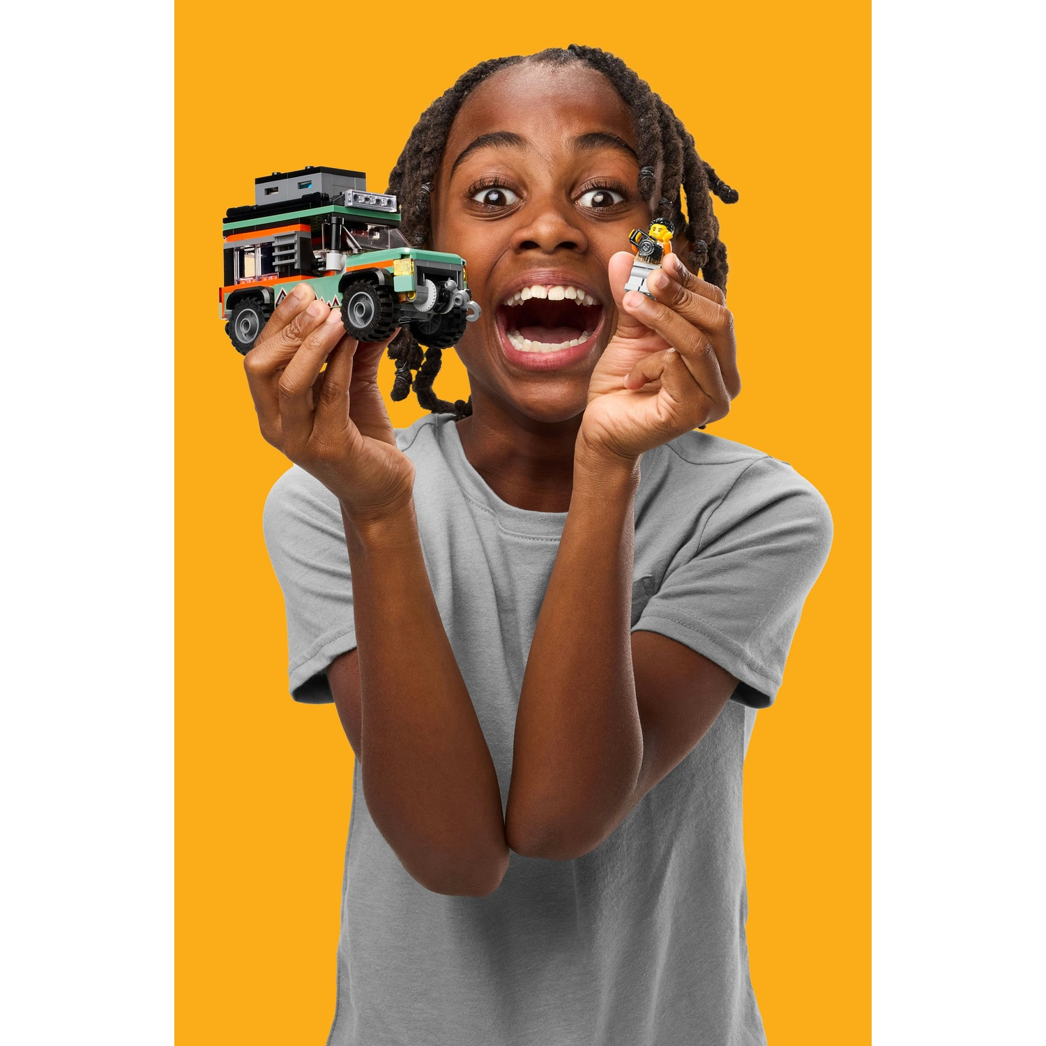 Un bambino tiene in mano un camion Lego e una figura Lego con espressione eccitata su sfondo giallo.