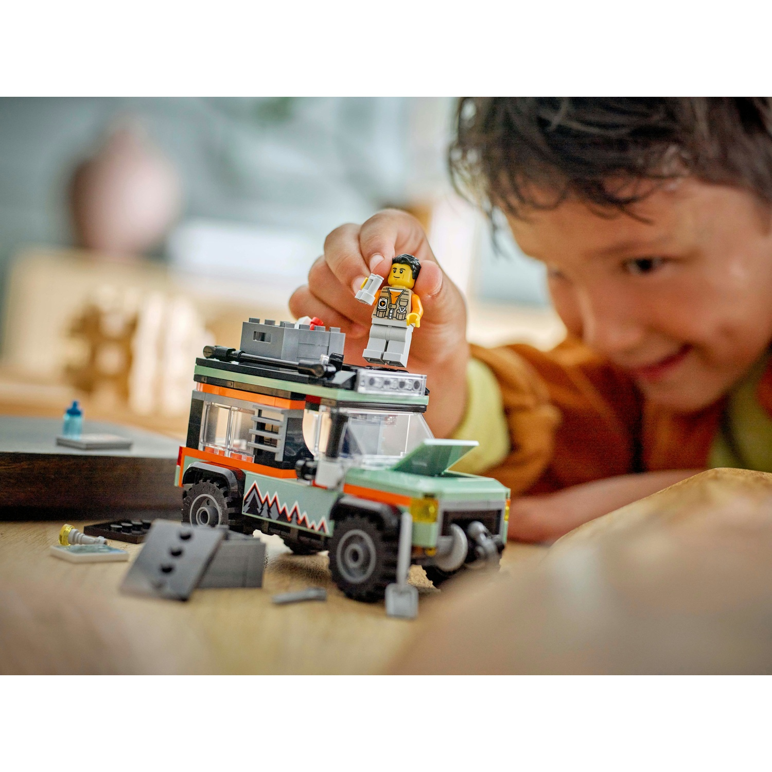 Un bambino gioca con un veicolo Lego. Il set Lego include un'auto fuoristrada verde e una minifigure in cima, con un bambino sorridente.