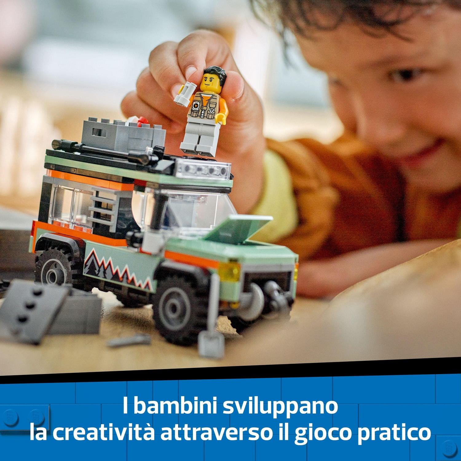 Un bambino gioca con un'auto Lego e un personaggio Lego. L'auto è verde e arancione. Il bambino sorride.