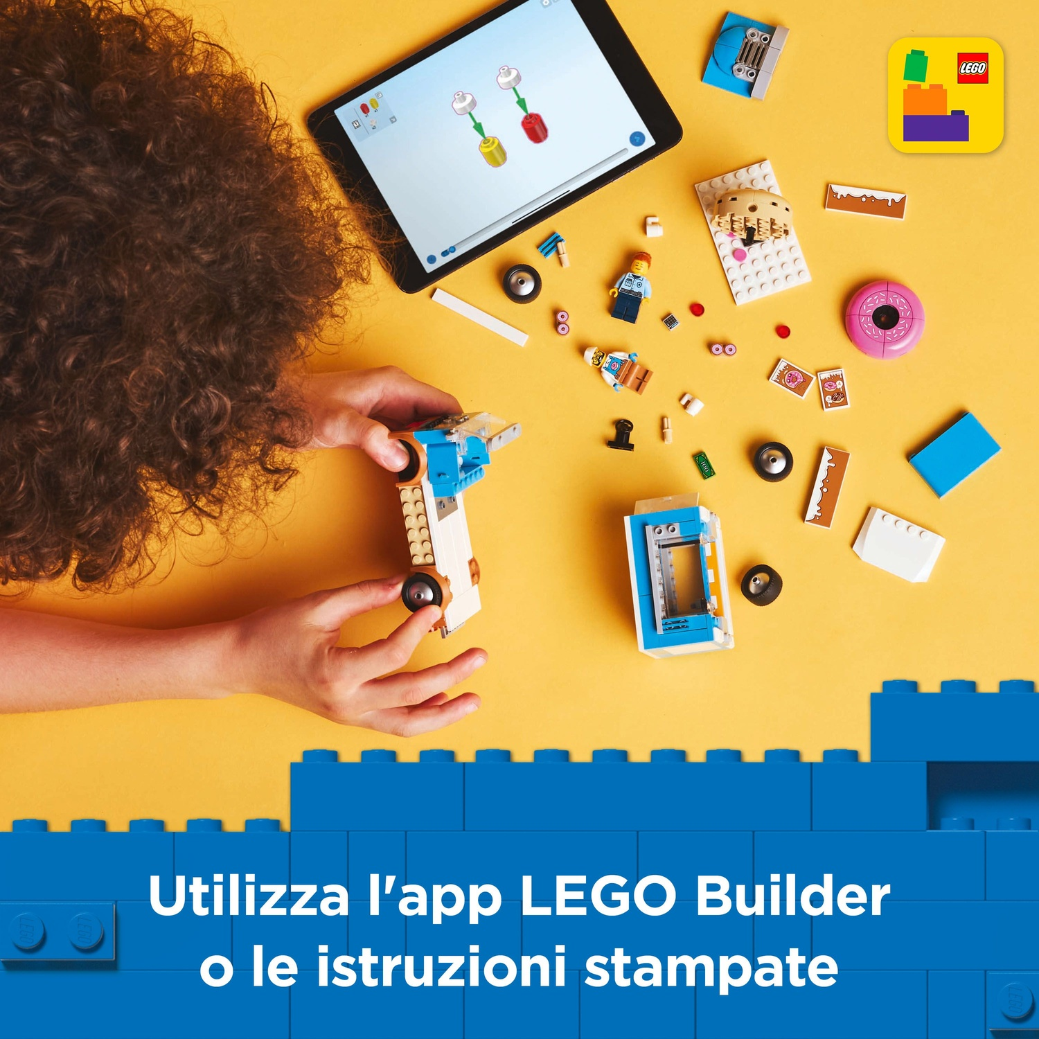 Un bambino costruisce con i LEGO. Un tablet mostra le istruzioni. Vari pezzi LEGO e un modello costruito sono su una superficie gialla.