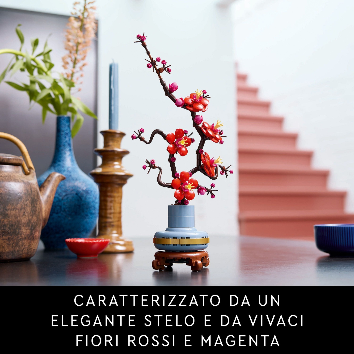 Un bonsai Lego con fiori rossi è su un tavolo. Vasi blu, una teiera e scale sullo sfondo.