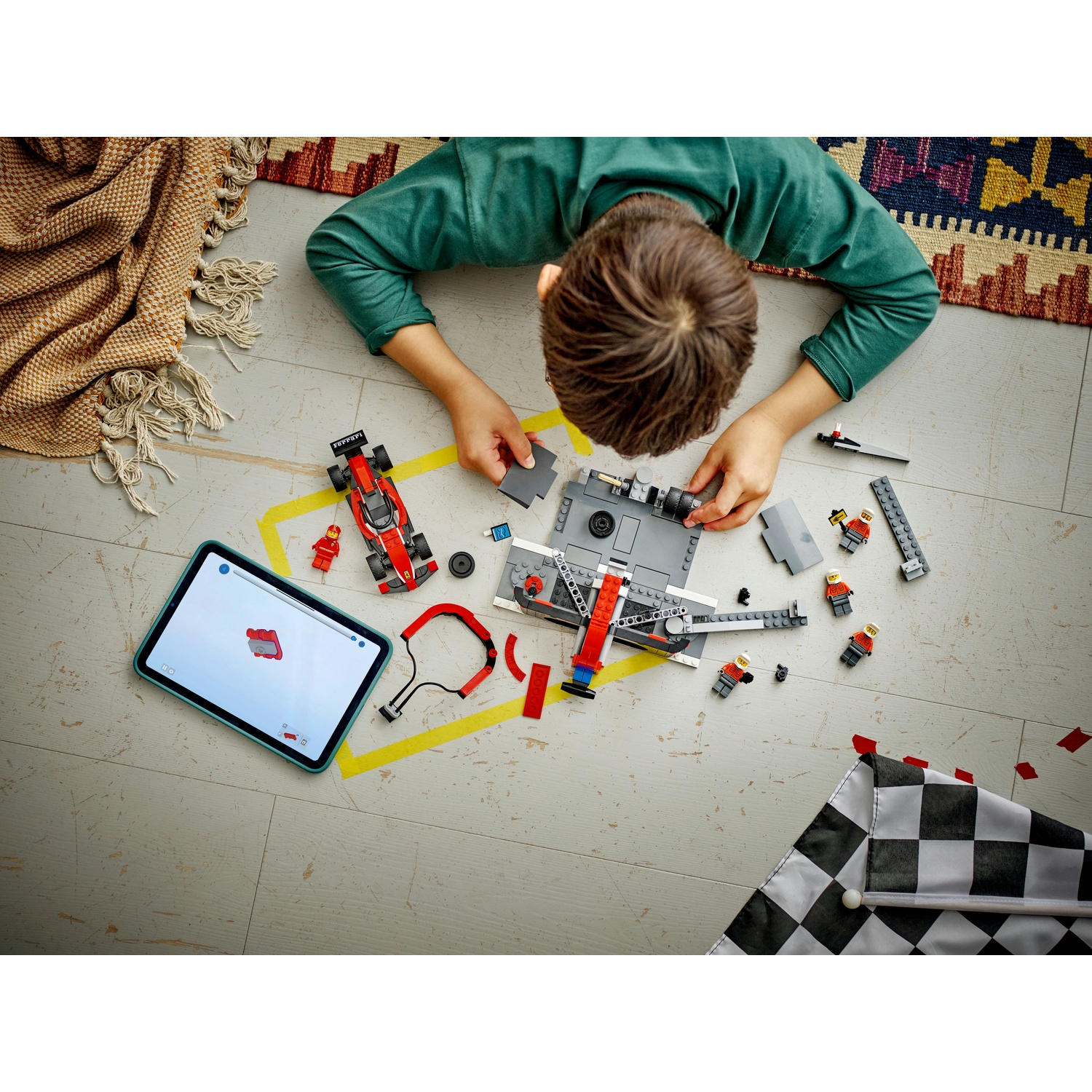 Un bambino sta costruendo un'auto da corsa Lego, seguendo le istruzioni su un tablet. La scena include una bandiera a scacchi e vari pezzi Lego.