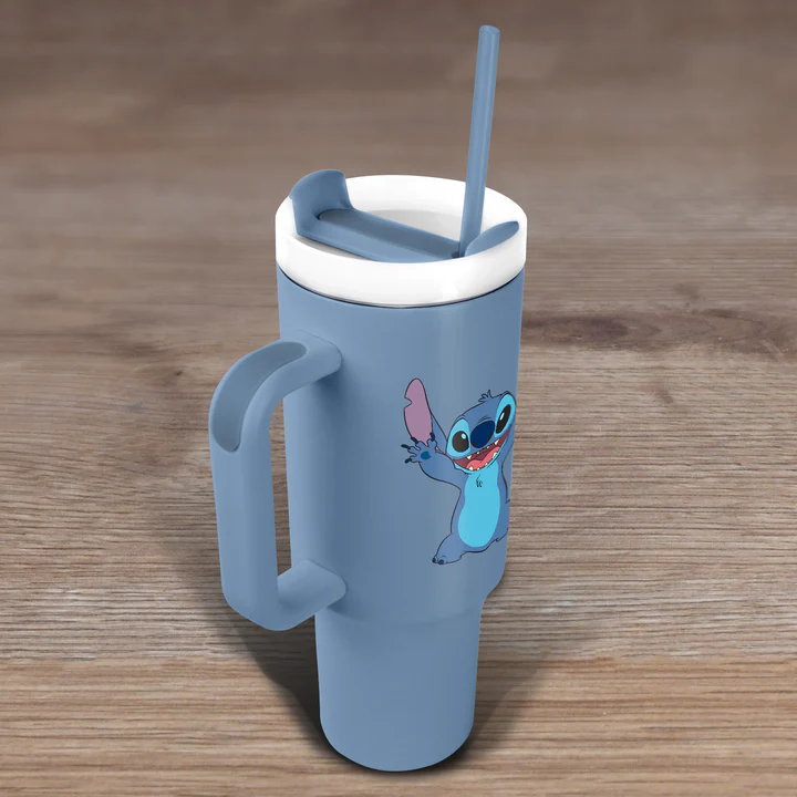 Vaso azul con diseño de Stitch, tapa blanca, asa y pajita sobre superficie de madera.