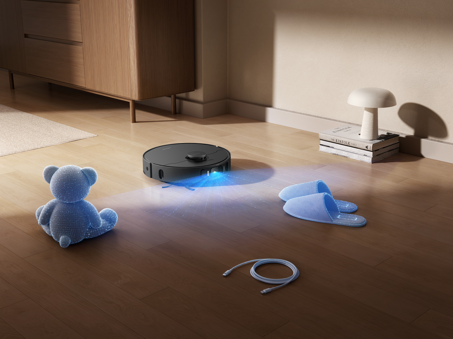 Una aspiradora robot en suelo de madera, cerca de un oso de peluche azul, zapatillas, una lámpara y libros.