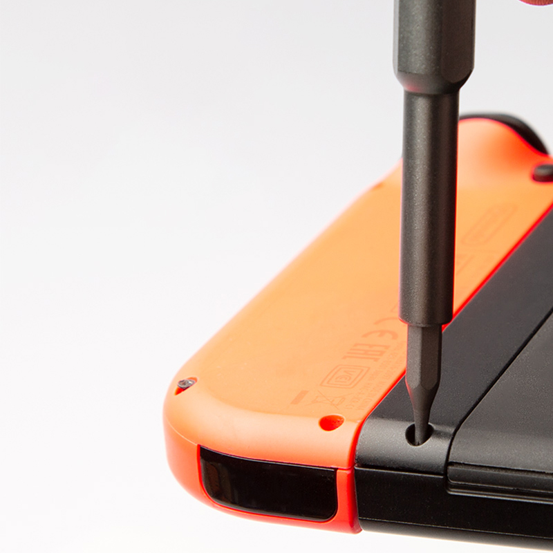 Turuncu bir Nintendo Switch Joy-Con kontrolcüsündeki siyah bir vidayı sökmek için bir tornavida kullanılıyor. Arka plan beyaz.
