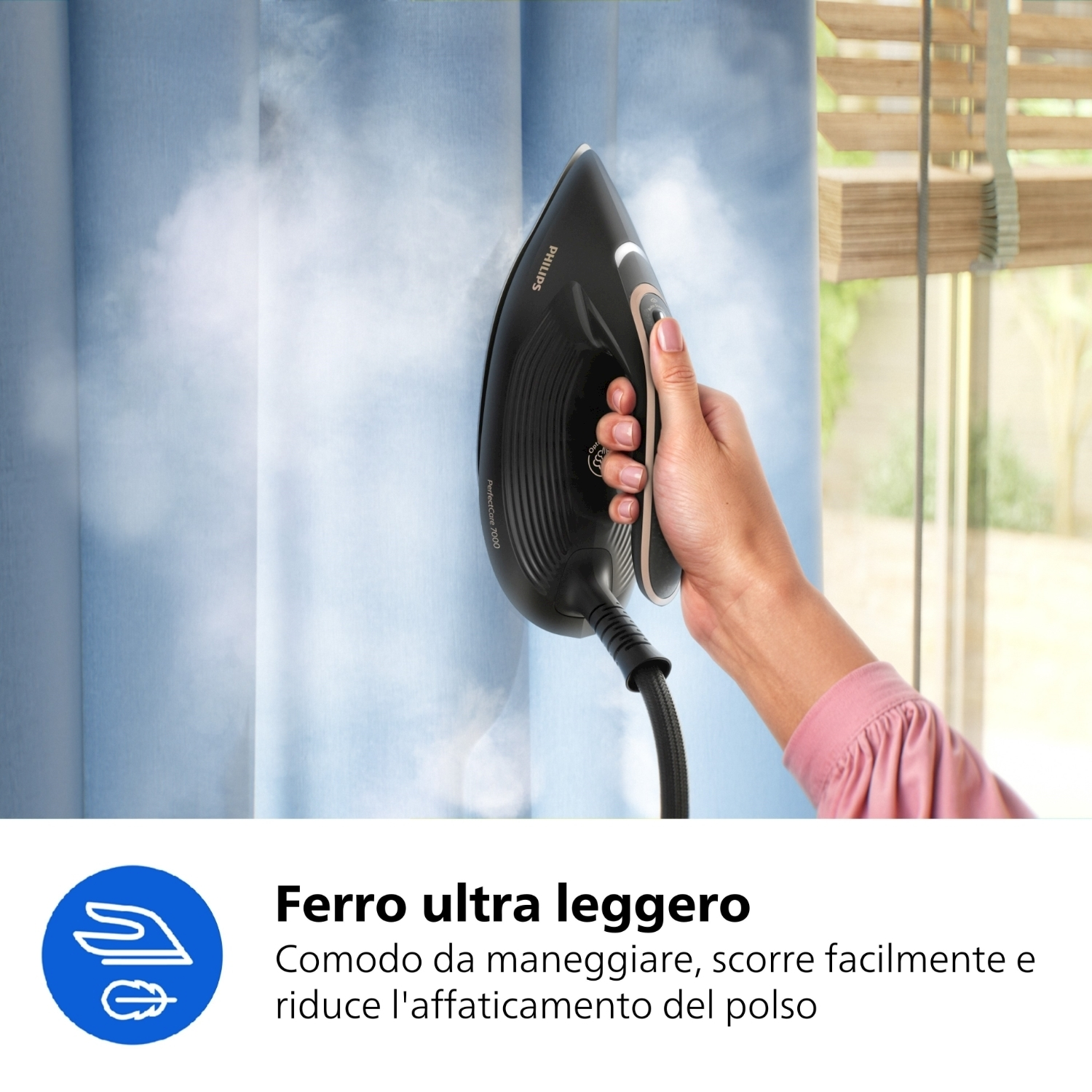 Una persona stira tende blu con un ferro da stiro Philips nero. Il vapore sale. Sullo sfondo c'è una finestra.