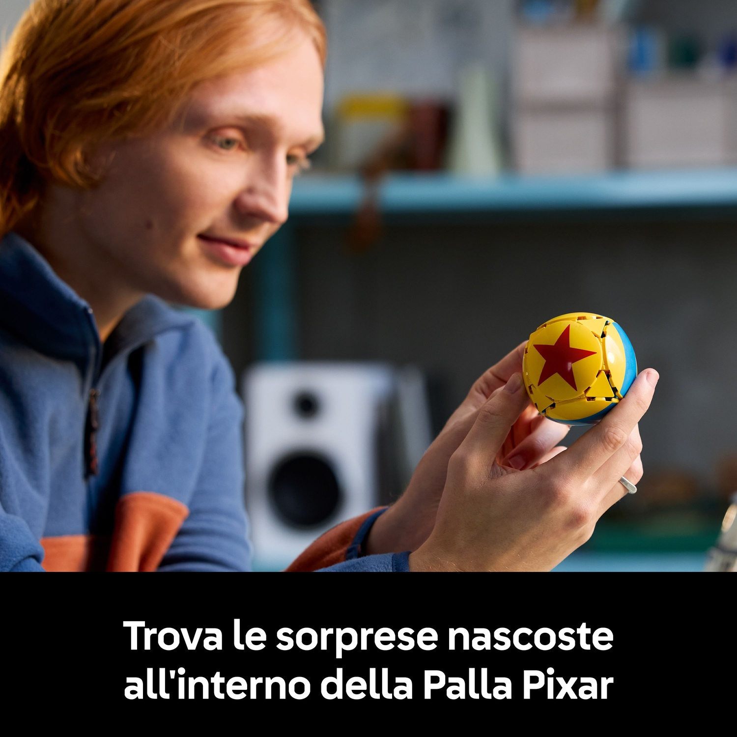 Una persona tiene in mano una palla Pixar. La palla è gialla con una stella rossa e sezioni blu. La persona indossa una giacca blu.