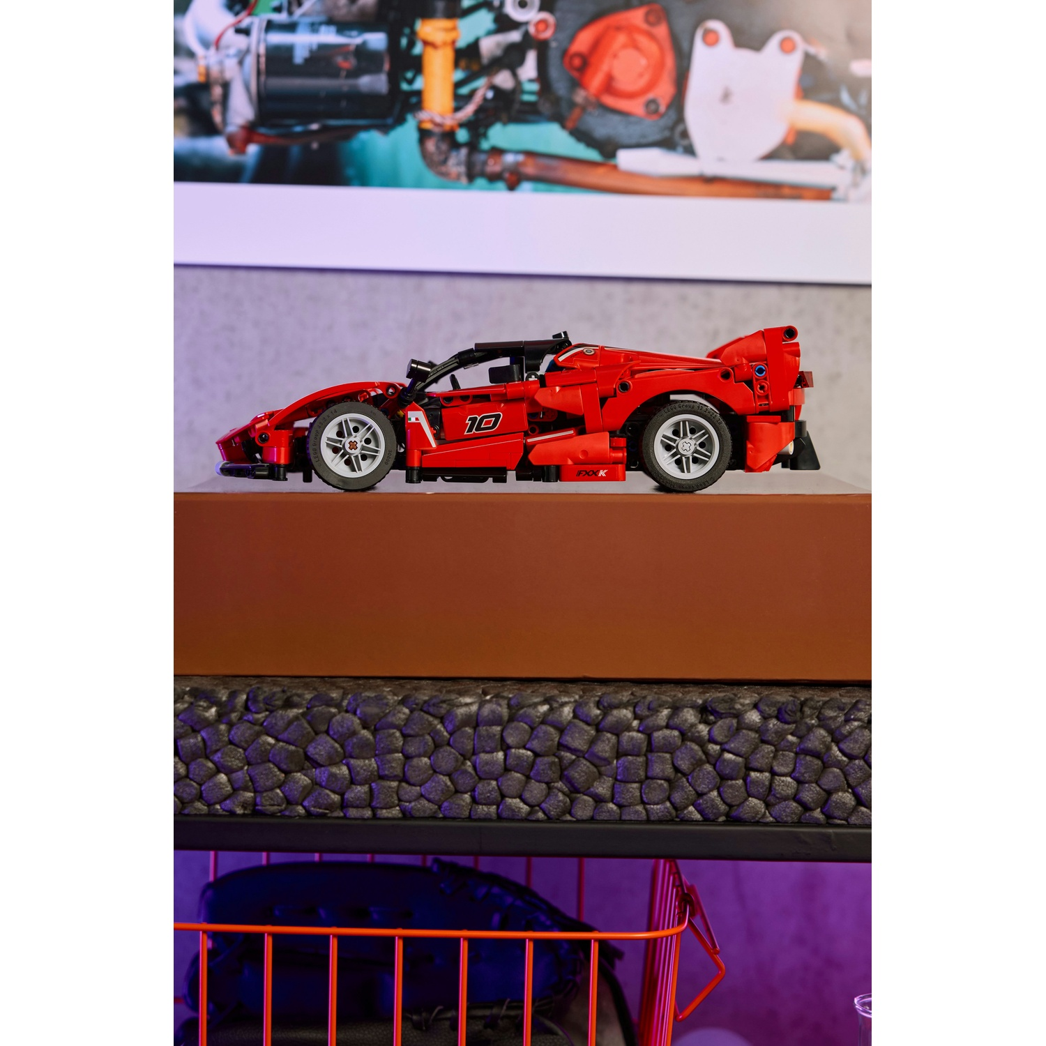 Un modello di auto sportiva Lego rosso è su uno scaffale. Sotto ci sono altri scaffali con una superficie nera e un cestino di filo arancione.